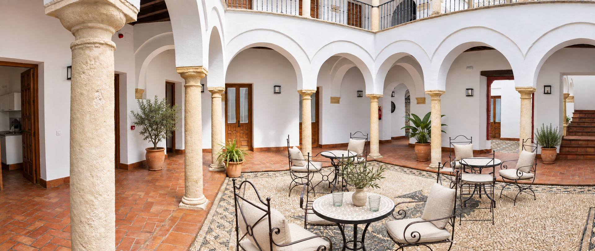 Sunlit courtyard with arches, stone columns, and café tables on a tiled terrace