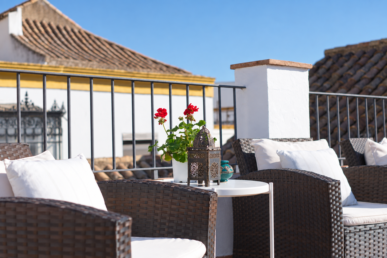 Patio seating with wicker chairs, white cushions, and a small table by a sunlit rooftop terrace.