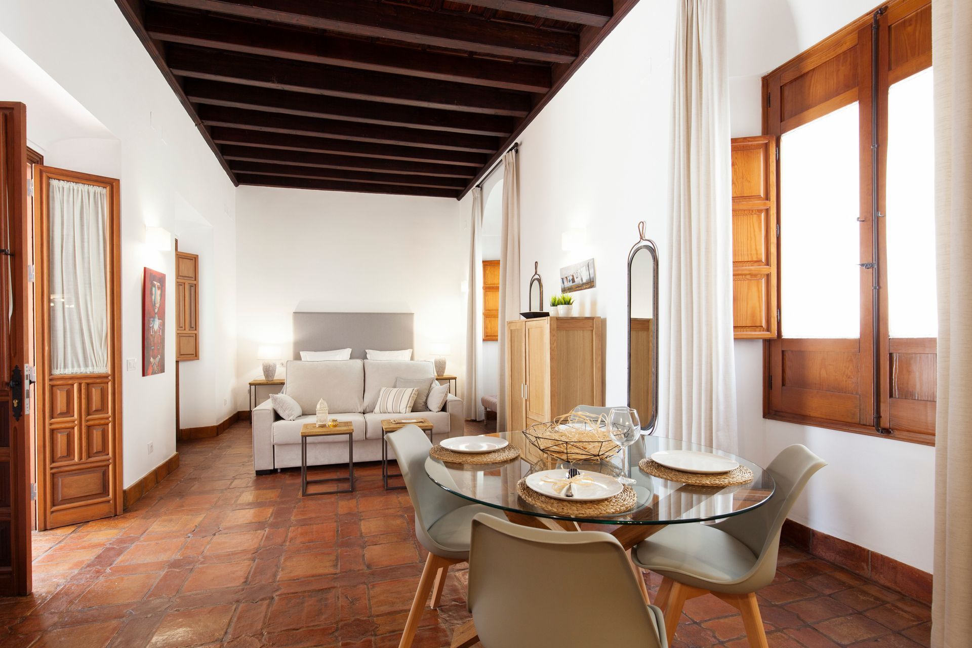 Bright dining and sitting room with wooden ceiling beams, white walls, and large windows, set for tea.