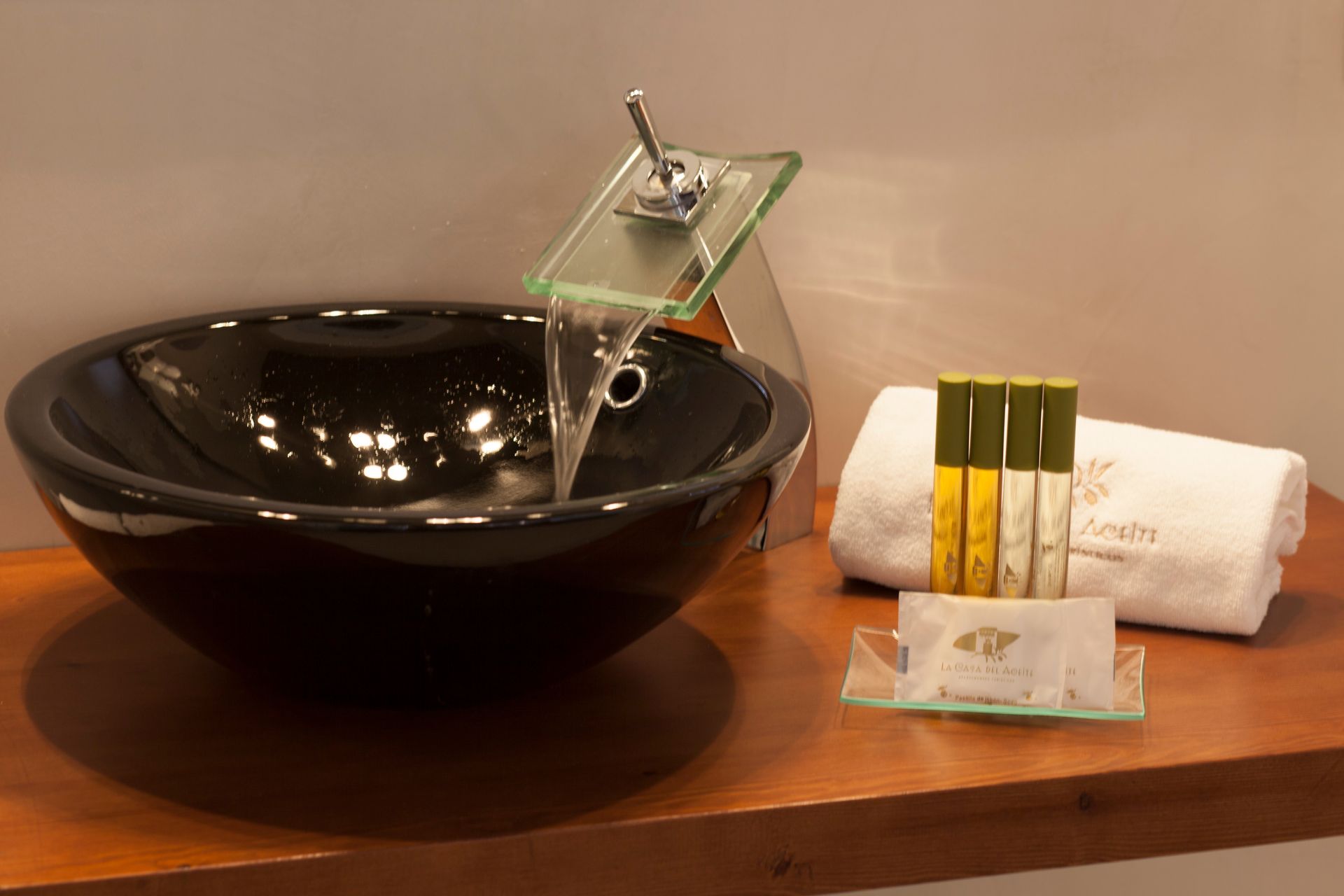 Spa tray with black bowl, glass water spout, and folded white towels on a wooden shelf