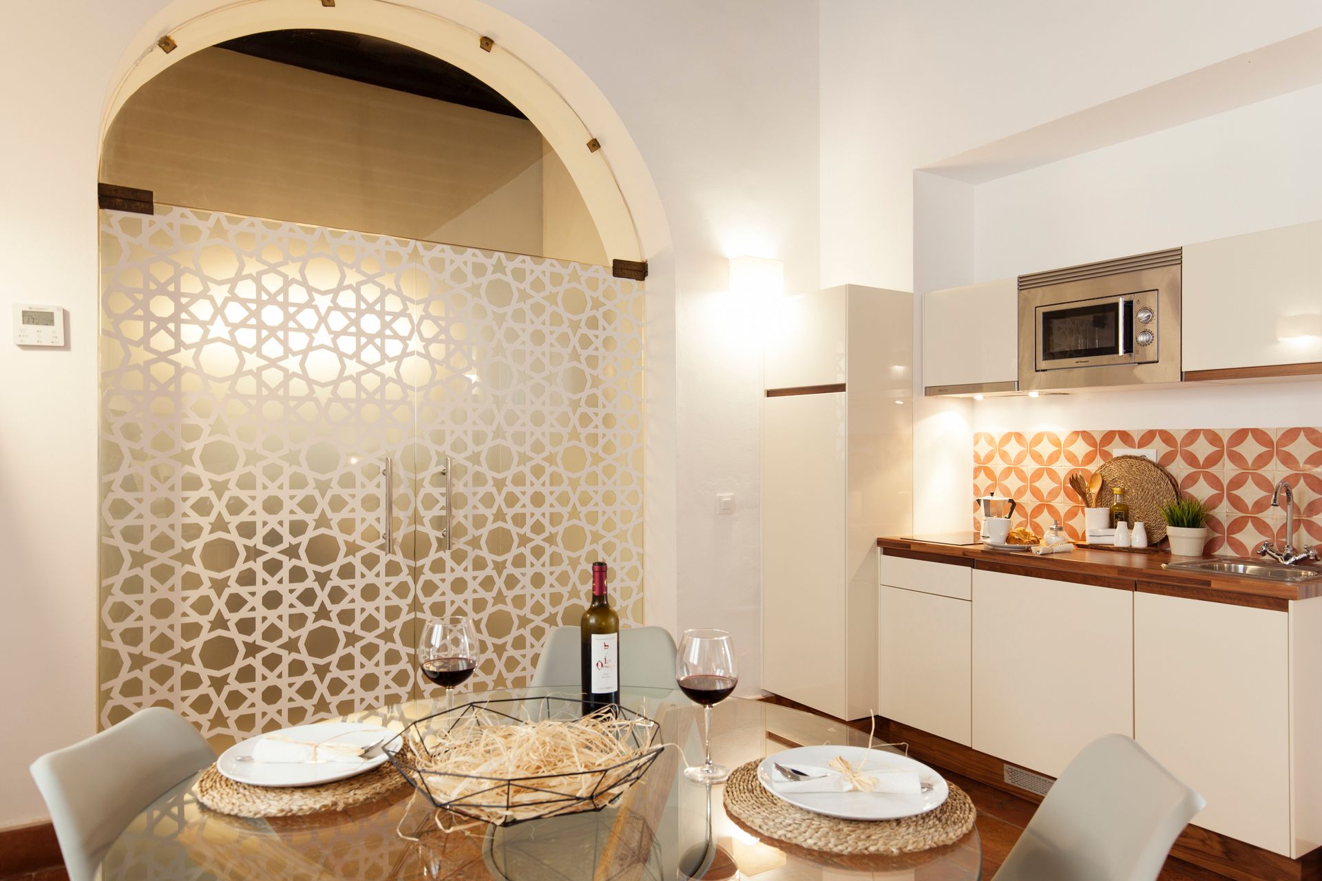 Modern dining area with arched partition, round table set for two, and a compact kitchen with warm lighting