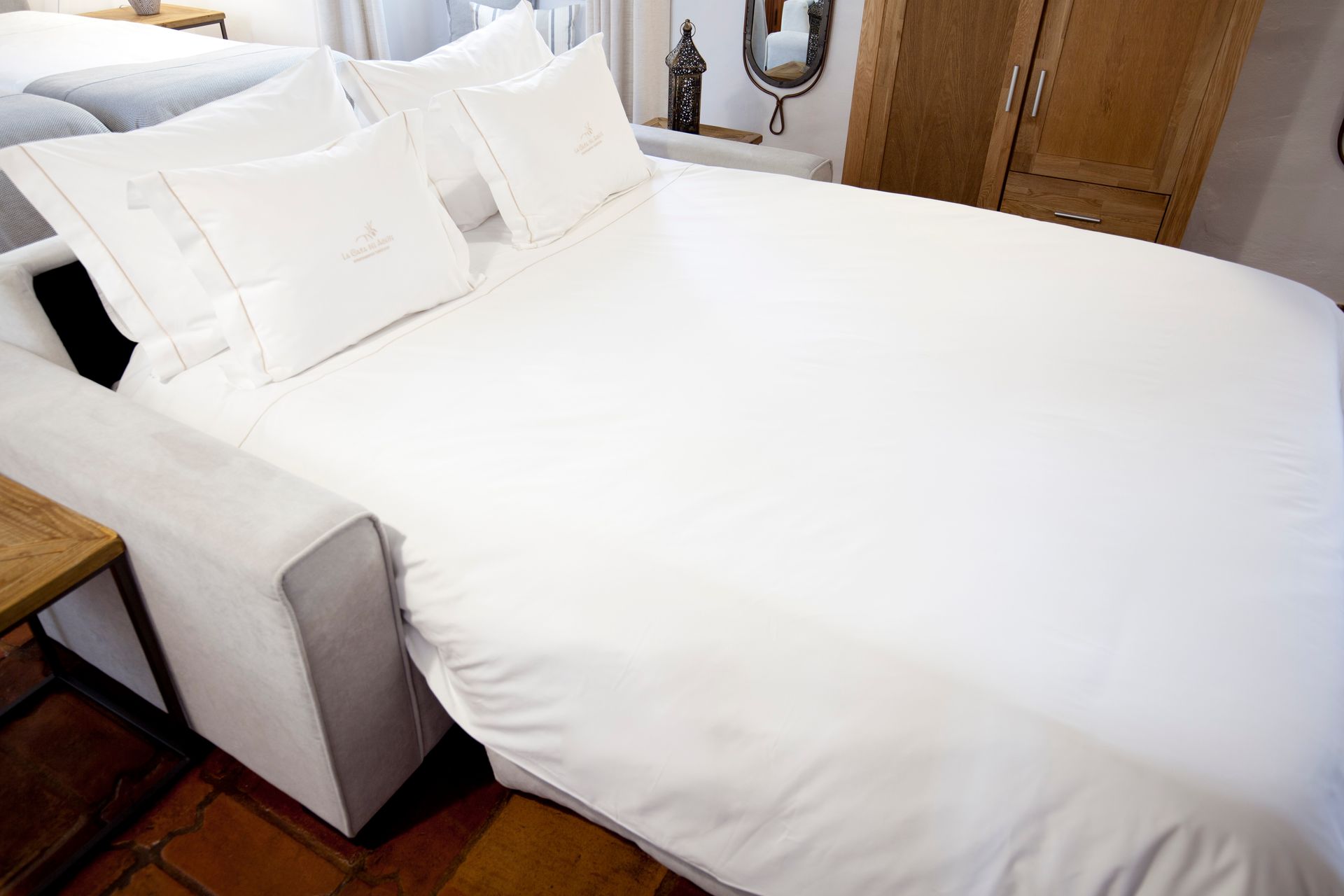 White bed with pillows and duvet in a cozy bedroom with wooden furniture and a mirror with lights