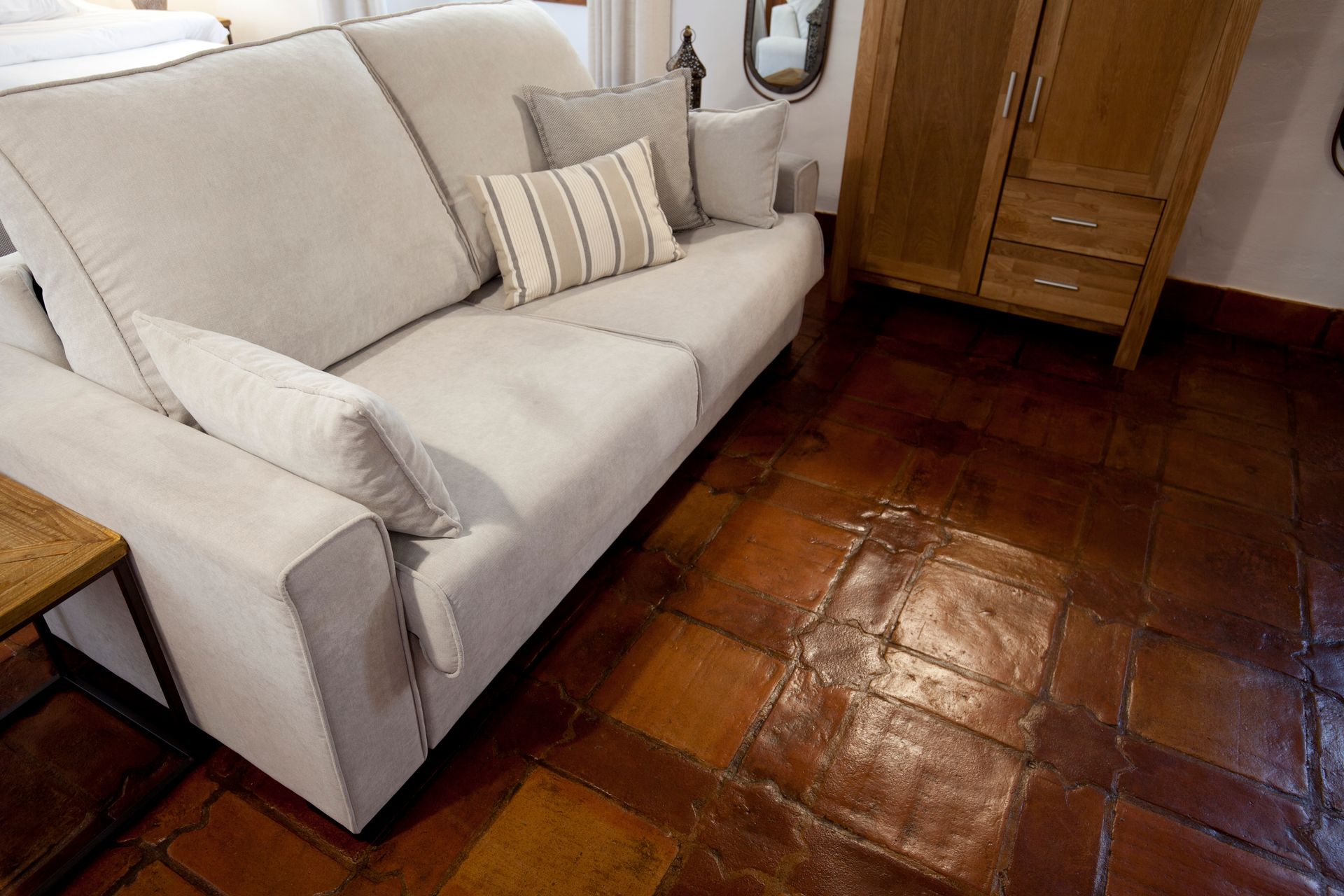 Cream sofa with striped pillow beside a wooden cabinet on a glossy tiled floor.