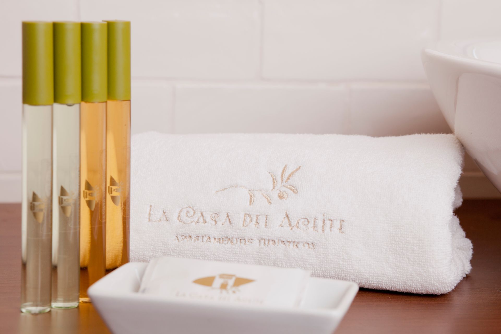 Spa toiletries with gold-capped bottles, folded white towel, and soap dish on a wooden counter