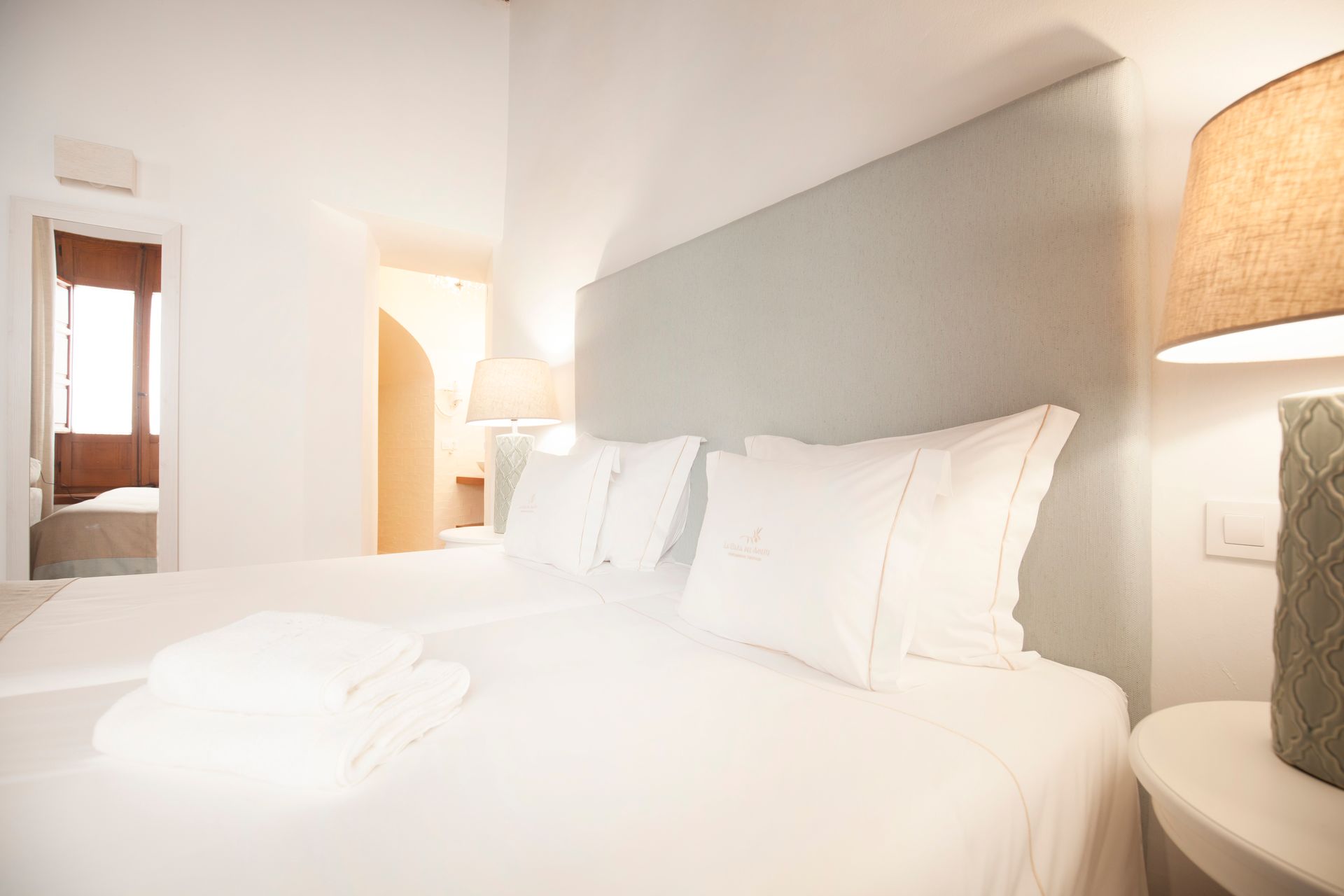 Bright white hotel bedroom with a neatly made bed, bedside lamp, and sloped ceiling