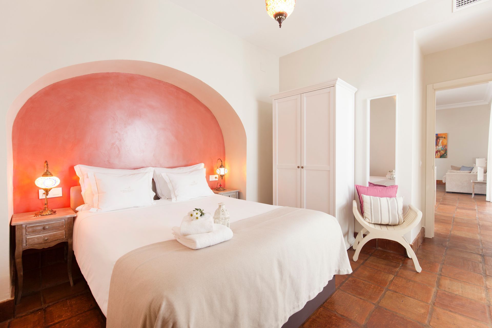 Cozy bedroom with coral accent wall, white bed, bedside lamps, wardrobe, and chair by the window