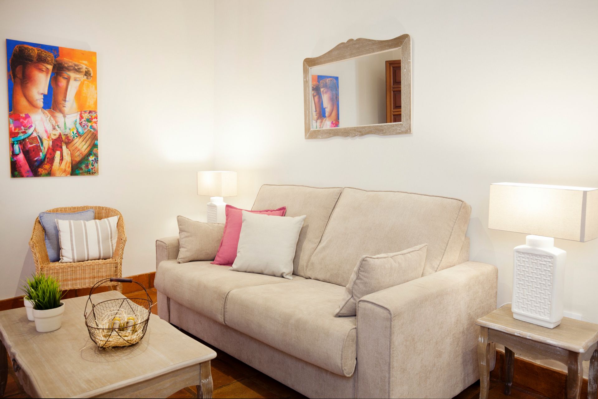 Cozy living room with beige sofa, lamps, coffee table, wicker chair, and colorful wall art