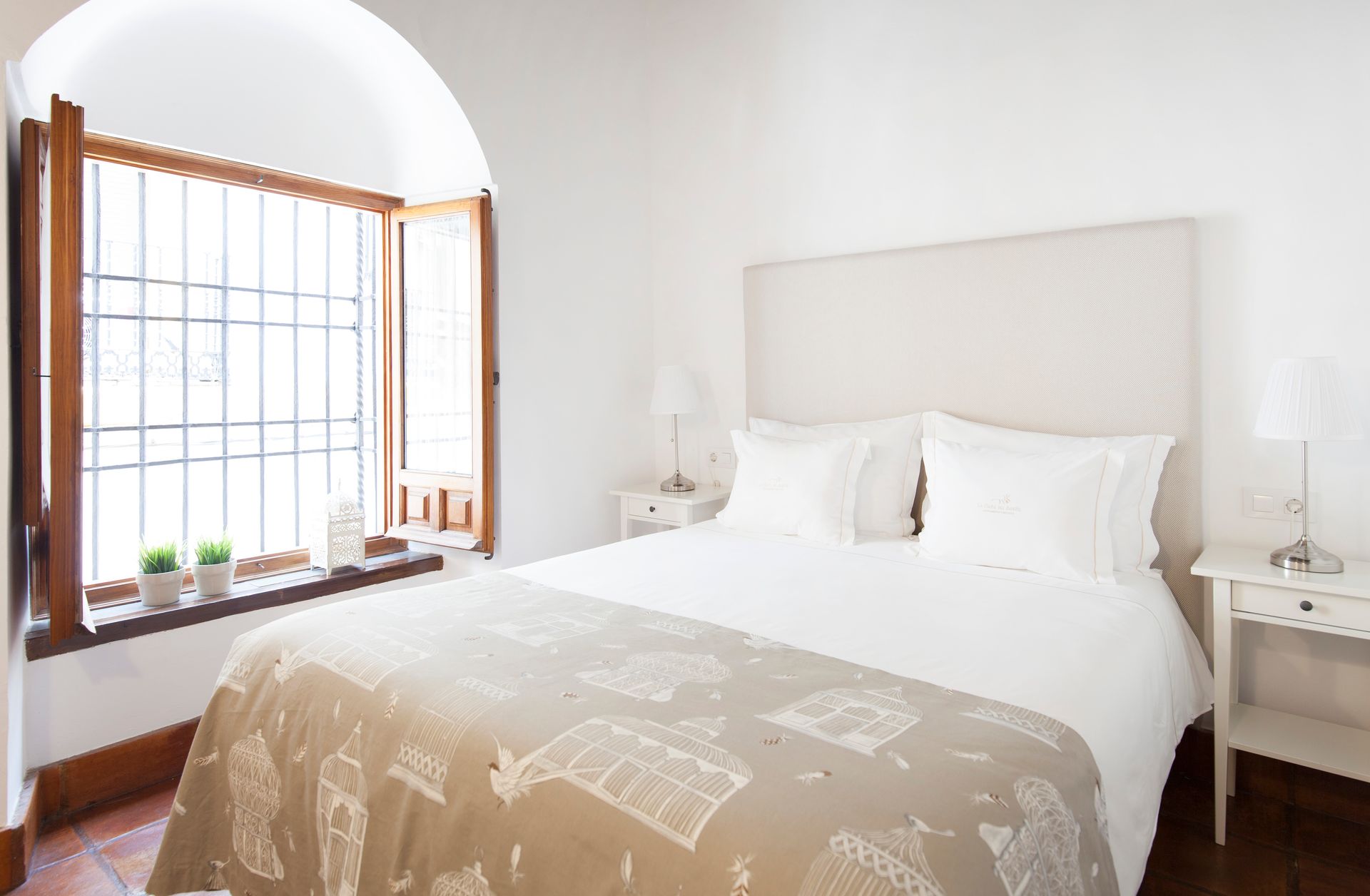 Bright bedroom with a white bed, wooden window seat, and beige throw blanket