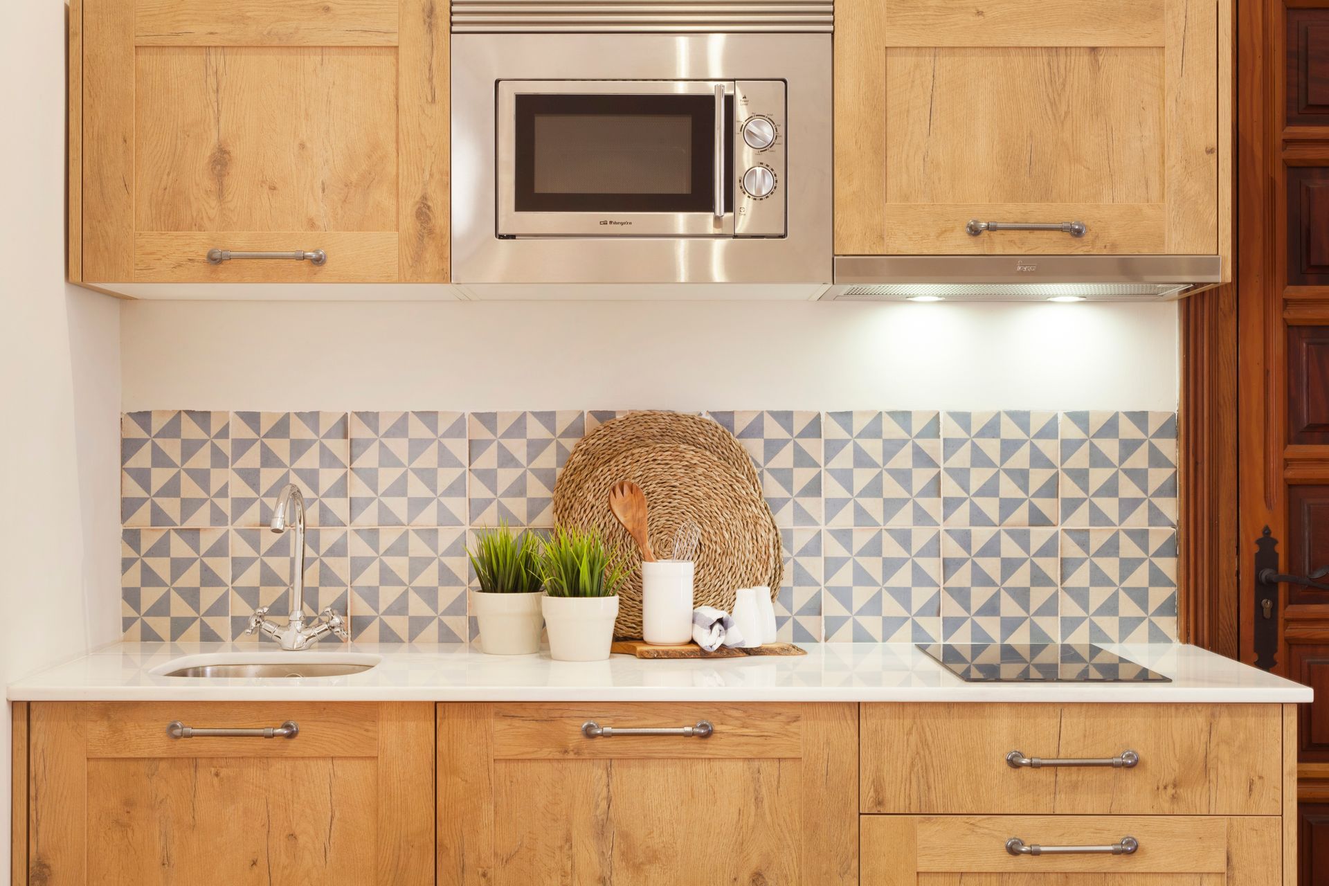 Modern kitchen with wooden cabinets, patterned backsplash, microwave, and countertop decor