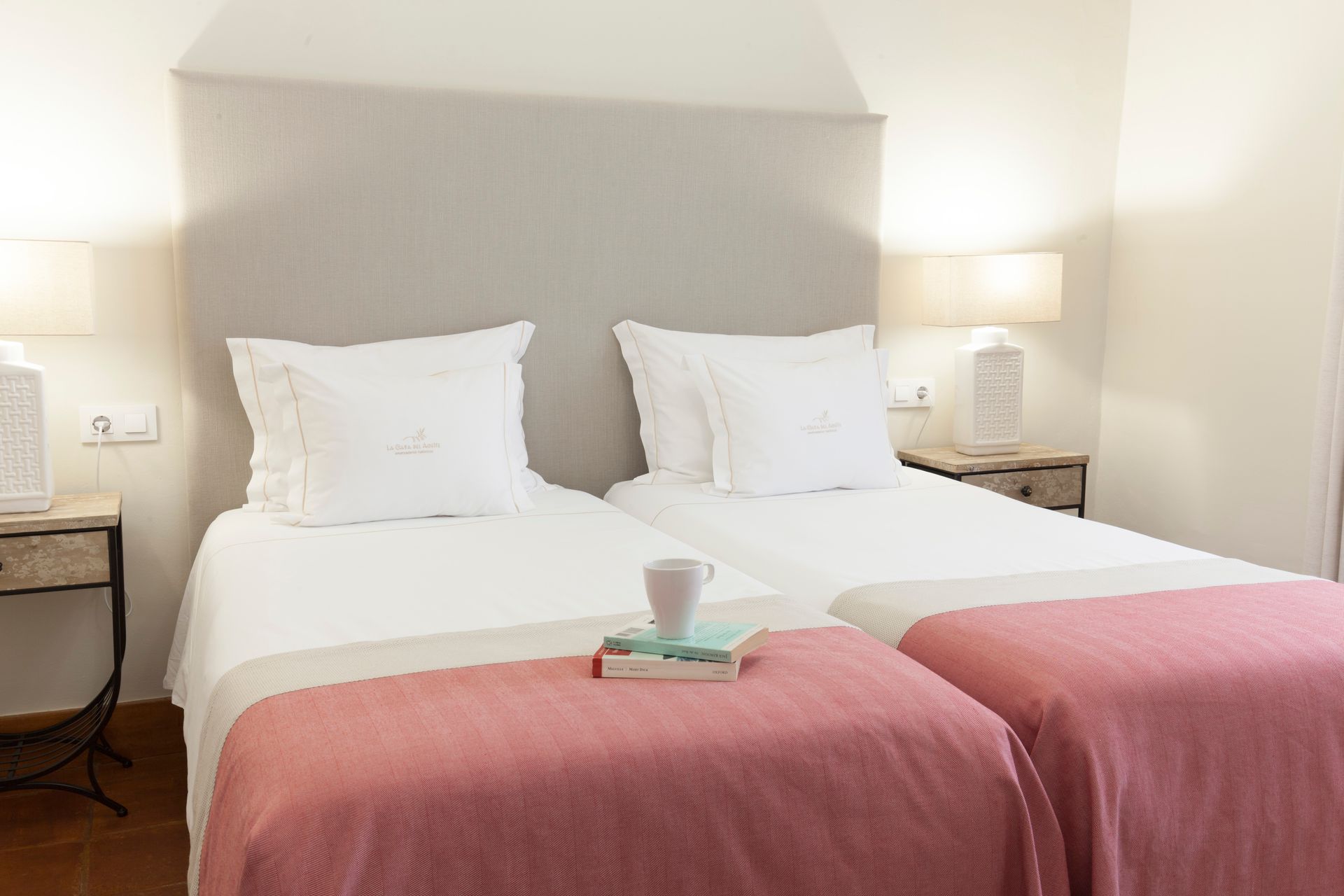 Twin beds with white linens and pink throws in a bright hotel room