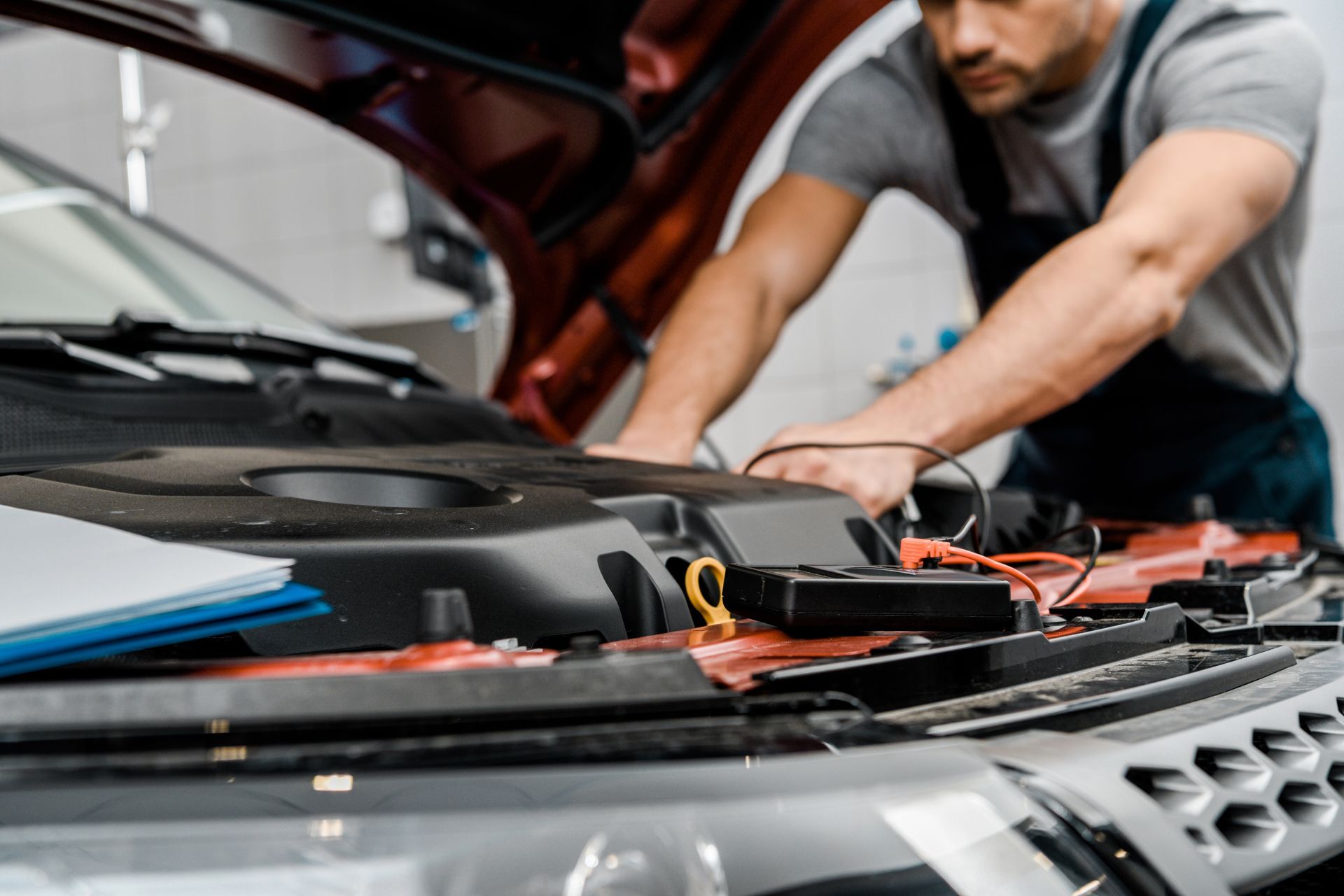Un meccanico utilizza un multimetro per controllare il motore di un’auto  in officina.

