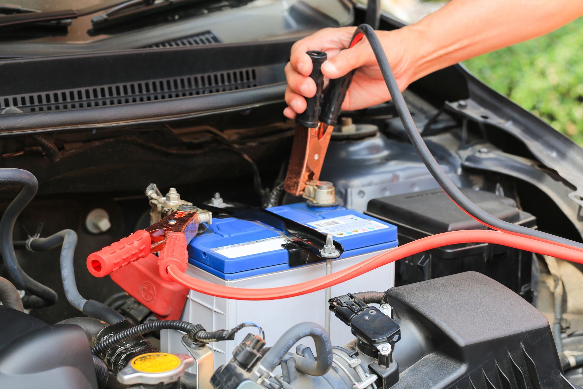 Una mano tiene una pinza nera per cavi di avviamento sopra il terminale della batteria dell’auto