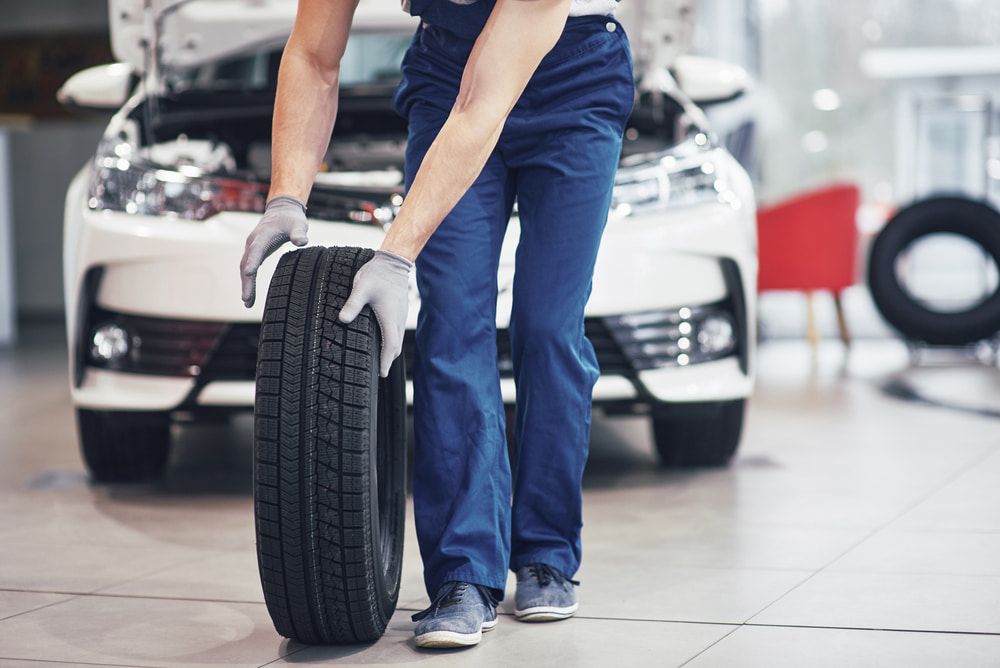 A Man Is Holding A Tire In Front Of A Car — Tonics Automotive in Garbutt, QLD