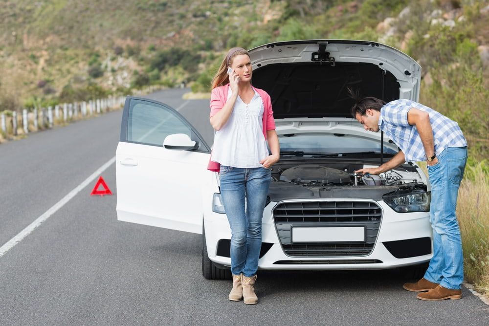 A Man And A Woman Are Standing Next To A Broken Down Car On The Side Of The Road — Tonics Automotive in Douglas, QLD