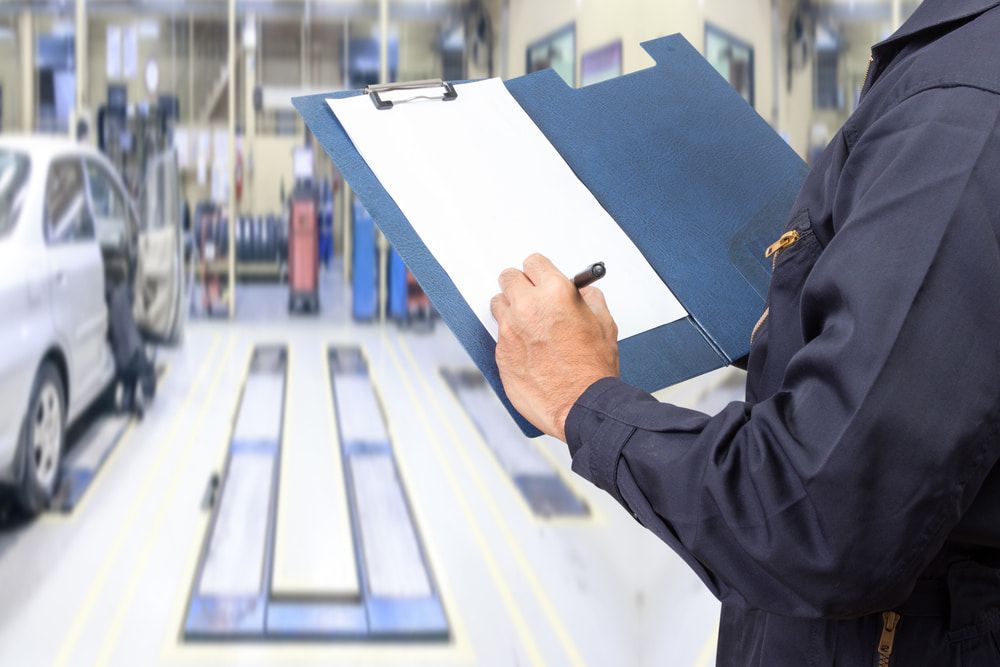 A Mechanic Is Writing On A Clipboard In A Garage — Tonics Automotive in Douglas, QLD