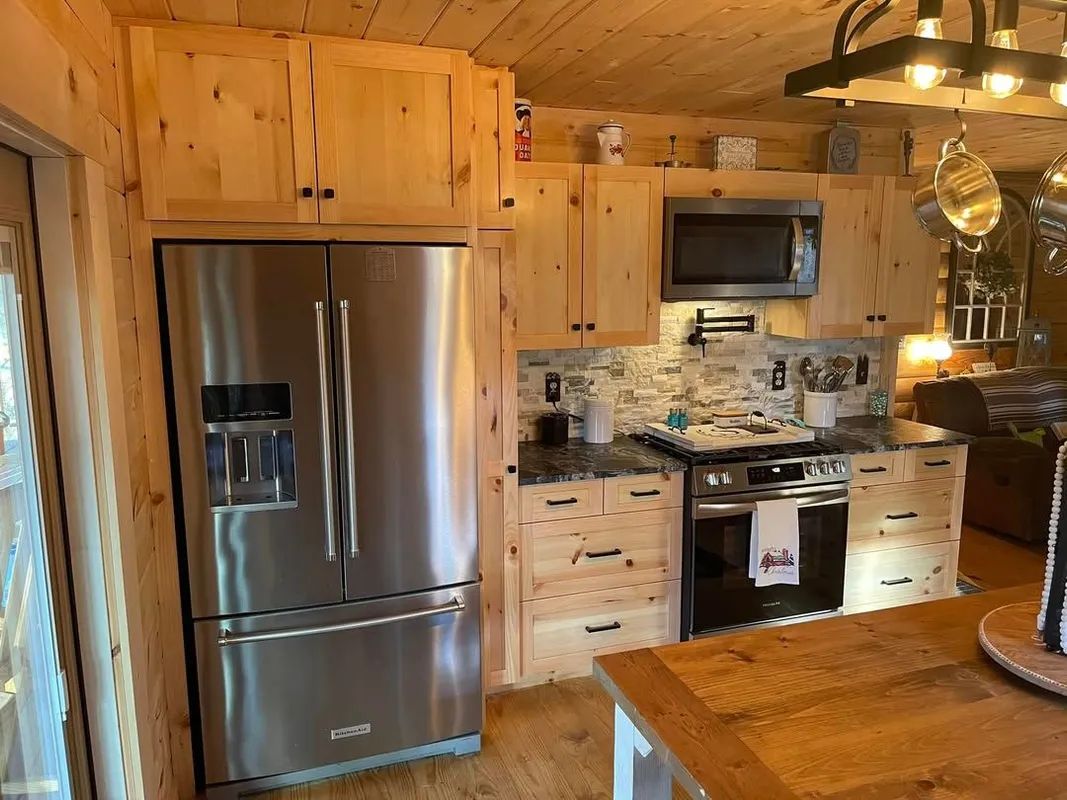 Cozy wood-paneled kitchen with stainless steel refrigerator, stove, and hanging pot rack