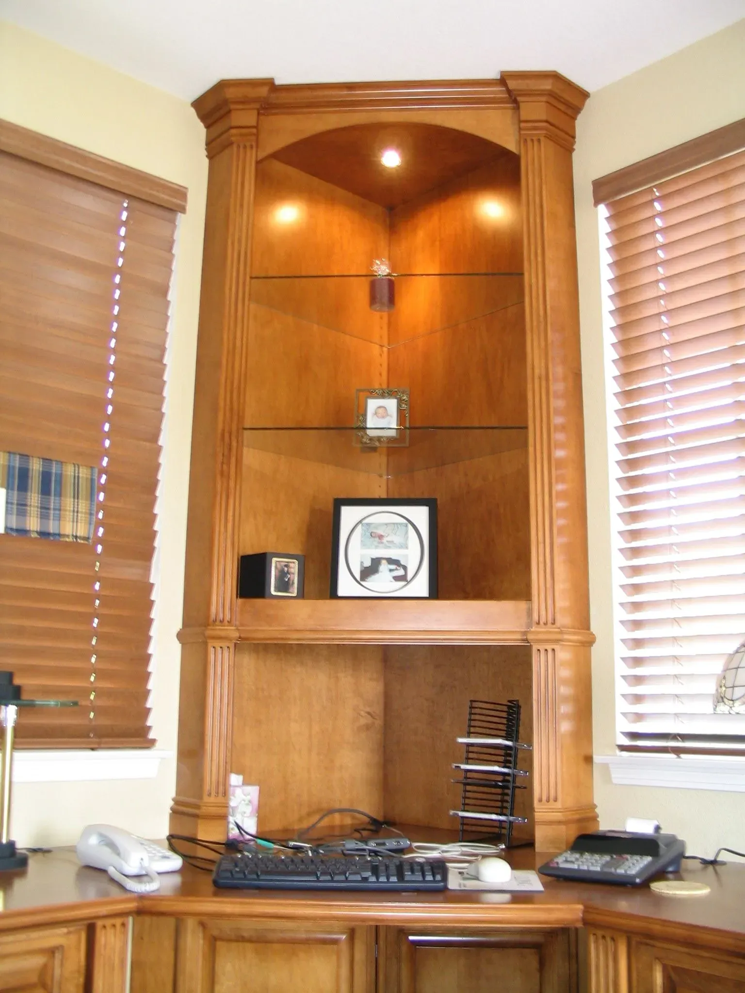Wooden office nook with built-in shelves, desk, blinds, and electronic equipment
