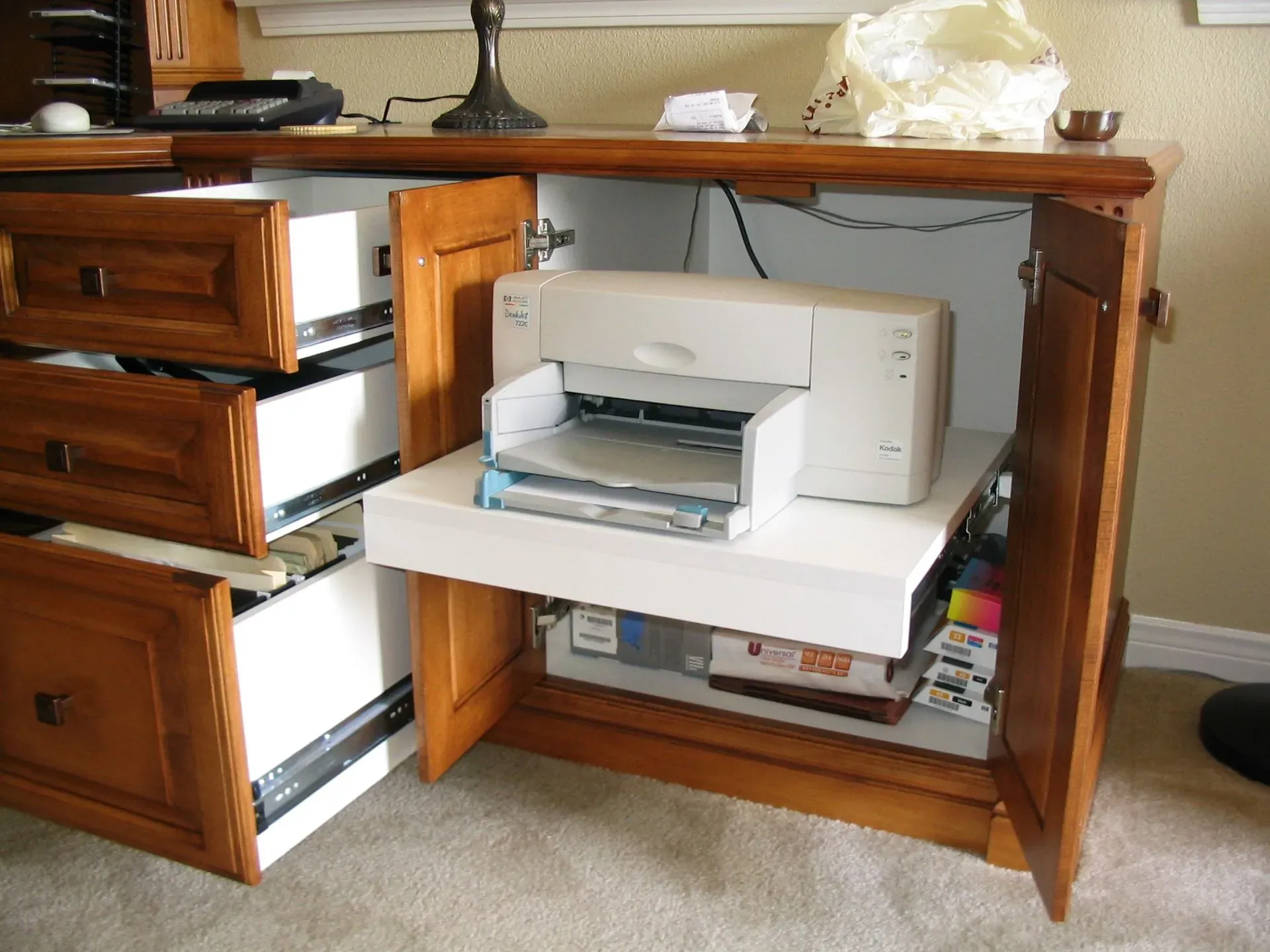 Wooden cabinet with drawers open, showing a white printer and office supplies inside.