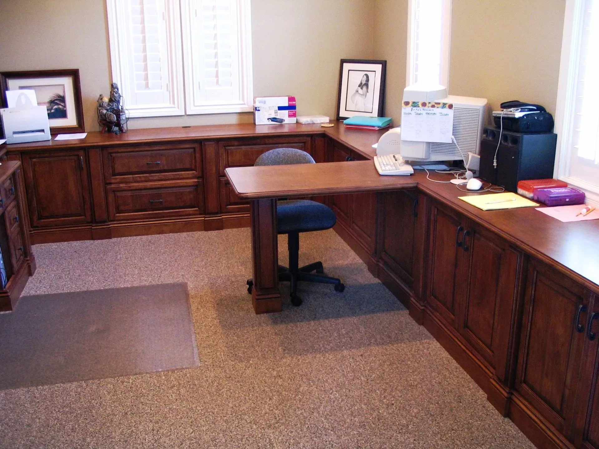 Office with wooden desk, computer, window, and chairs on a carpeted floor