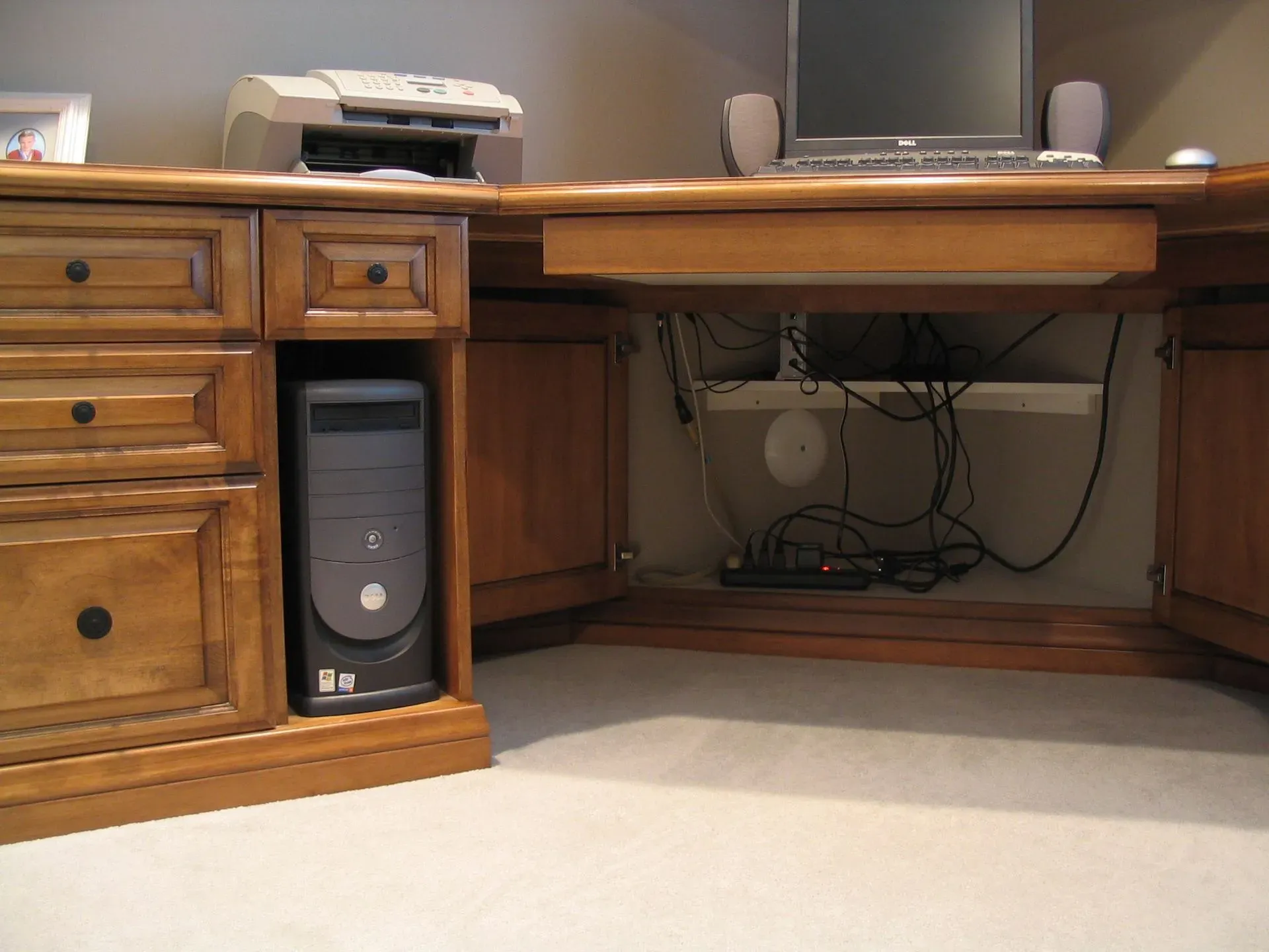 Wooden desk with drawers, printer, computer monitor, and a tower PC in a carpeted home office