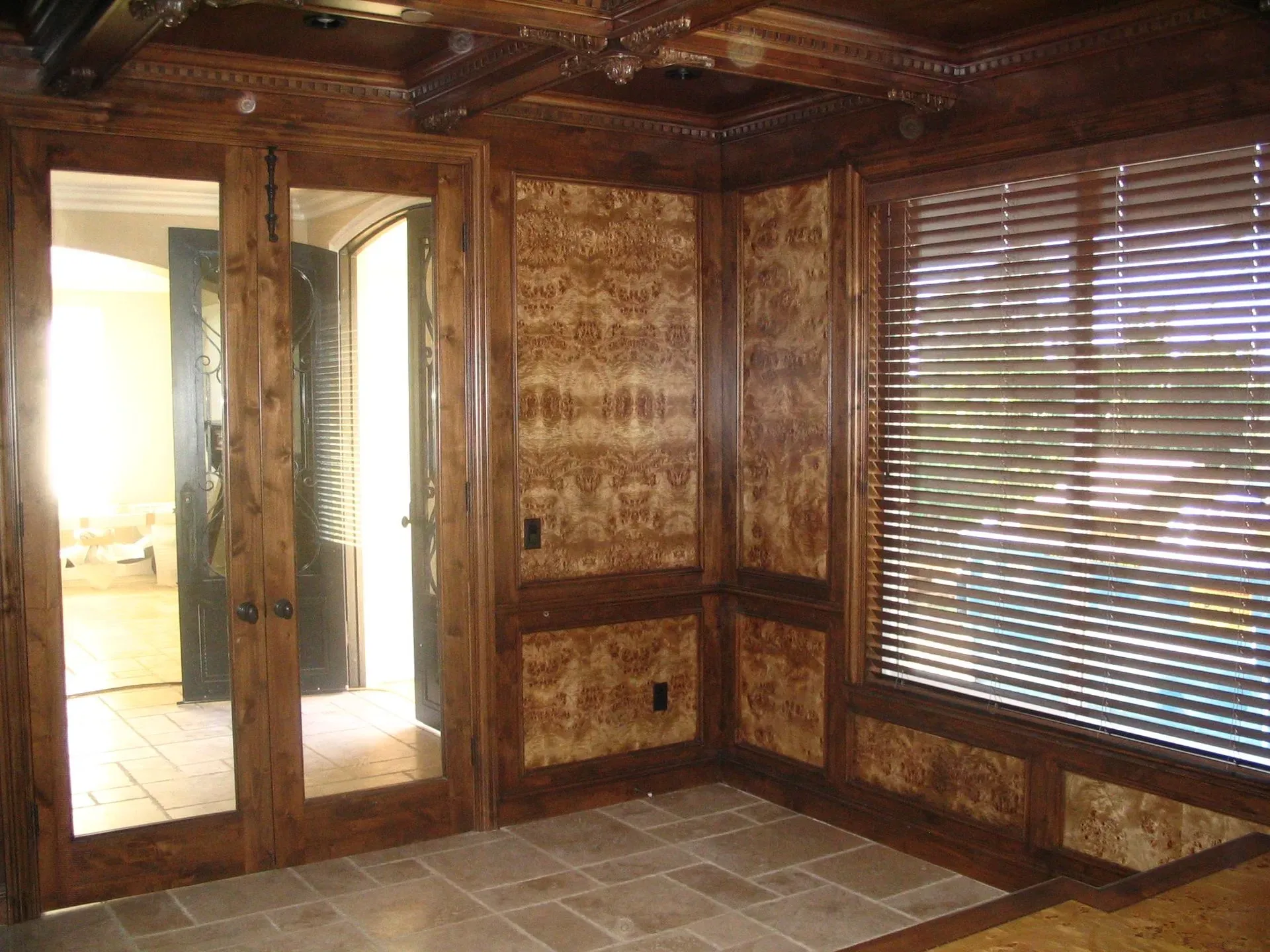Empty wood-paneled room with tiled floor, mirrored closet doors, and a large window with blinds