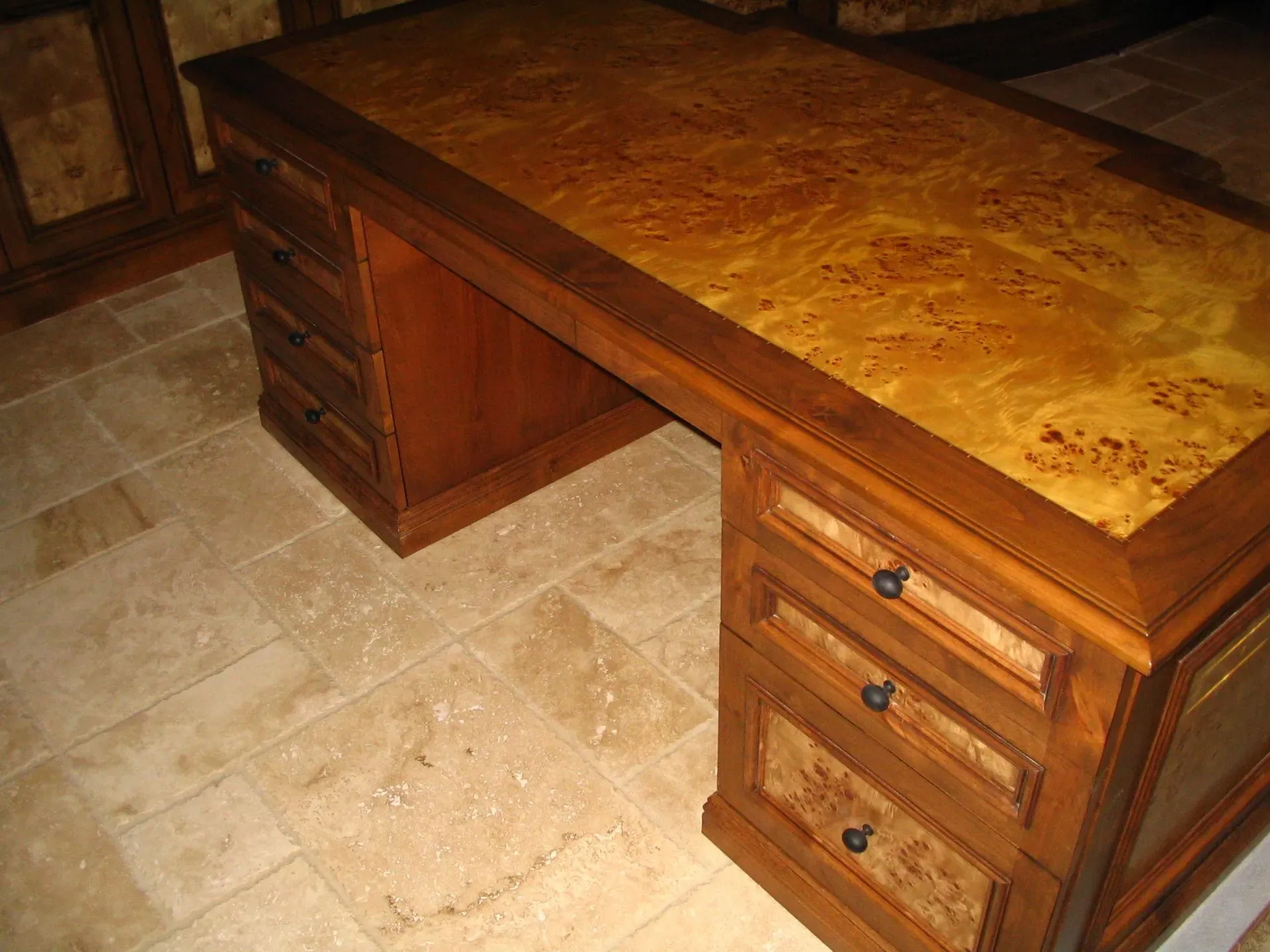 Wooden office desk with drawers and a glossy burl wood top on a tiled floor