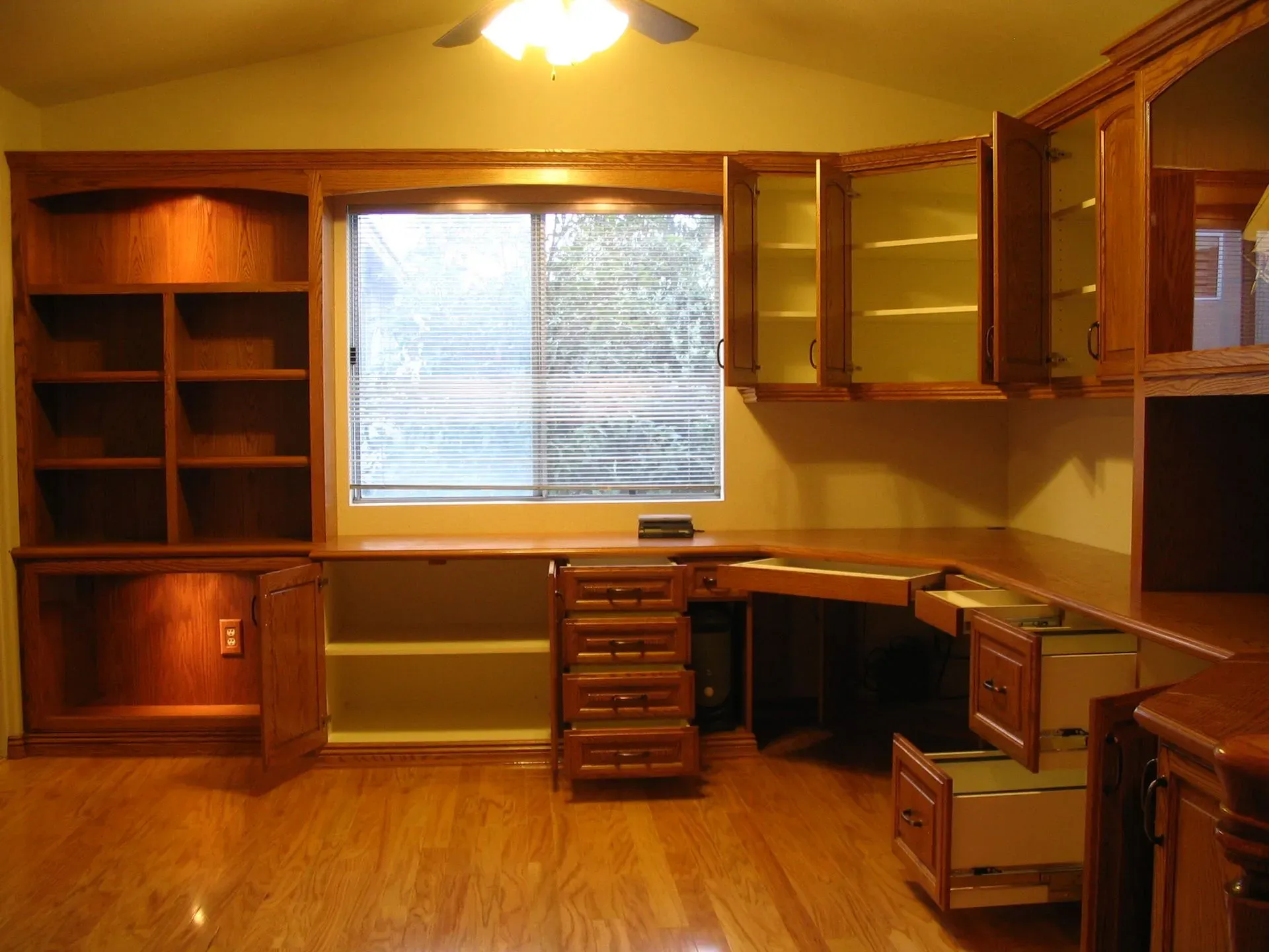 Wooden home office with built-in shelves, desk, drawers, and a central window.