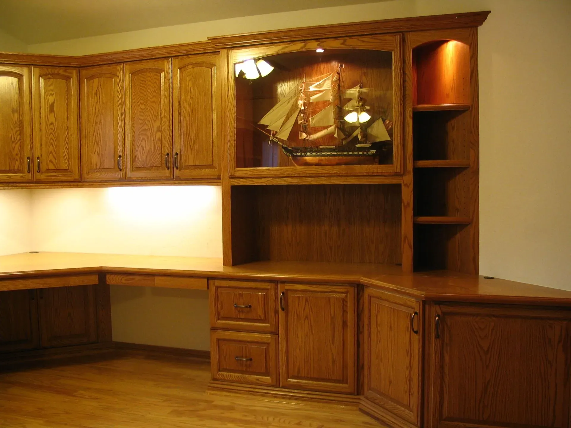 Wooden built-in home office cabinets with a desk, drawers, and glass display shelves