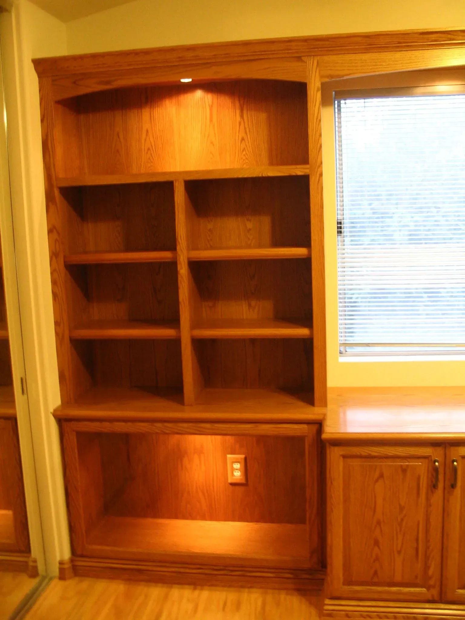 Built-in wooden shelves and cabinets beside a window with white blinds.