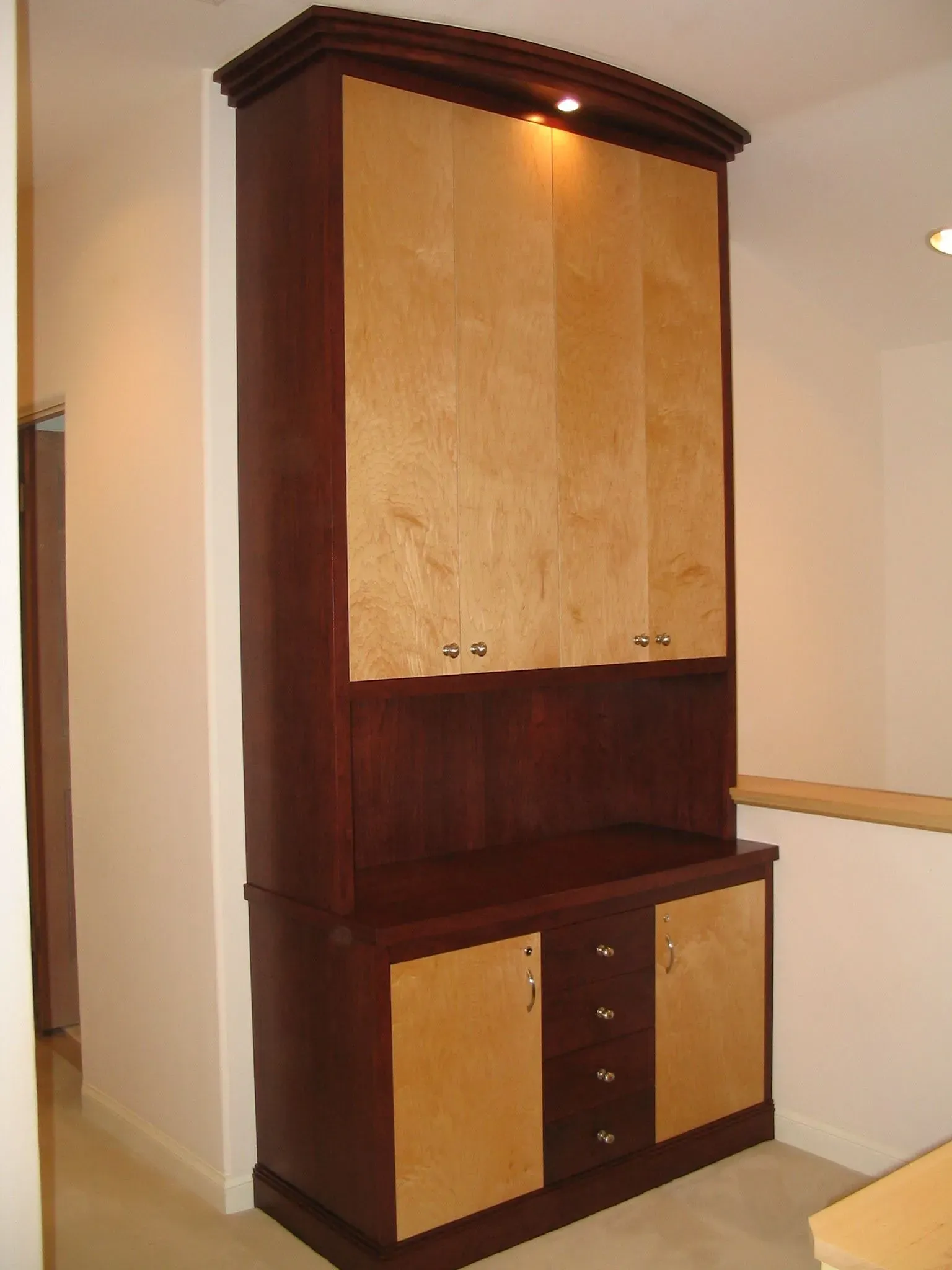 Tall wooden cabinet with light and dark wood panels in a hallway alcove.