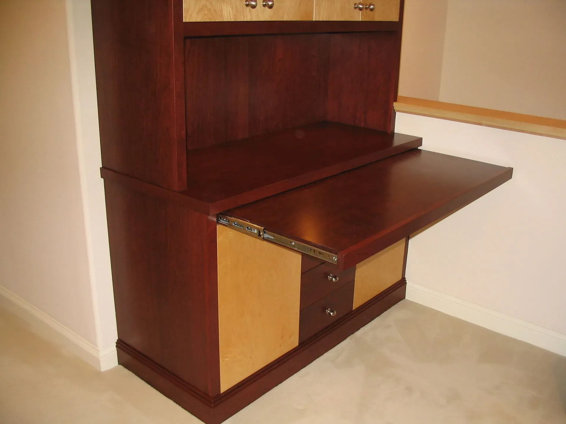Wooden wall-mounted desk with a pull-out writing shelf in a carpeted room