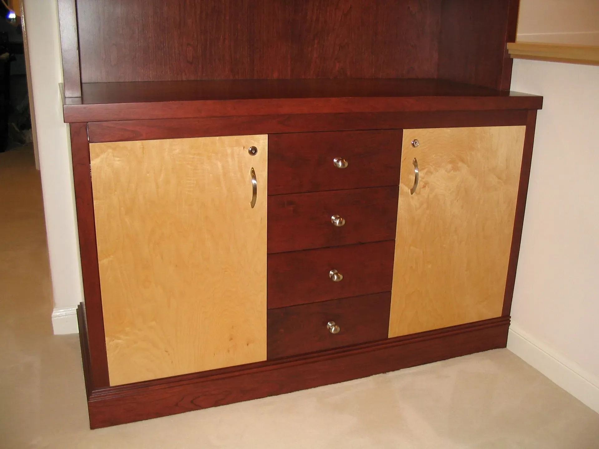Wooden cabinet with two light doors and four central drawers against a wall.