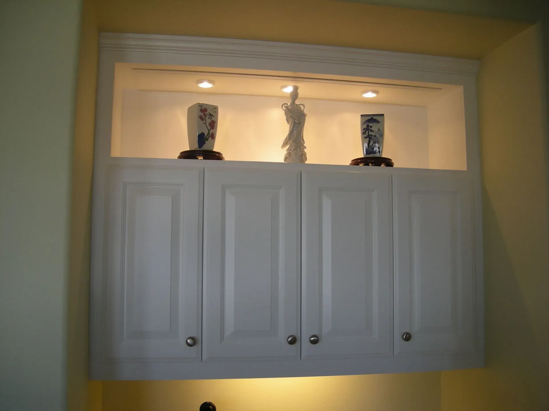 White cabinet with three decorative figurines displayed in a lit recessed alcove.