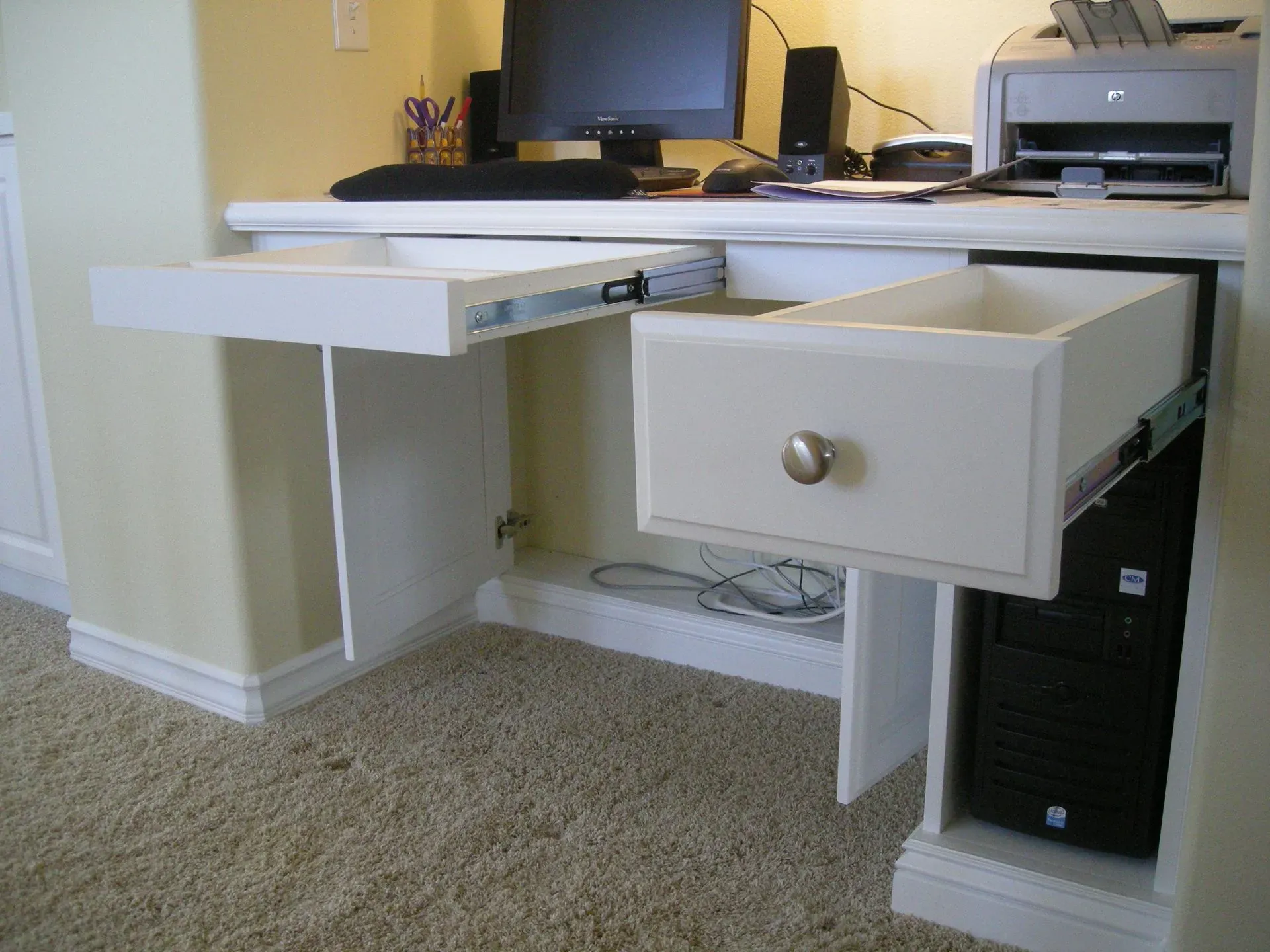 Desk with a computer, printer, and open drawer in a carpeted office corner