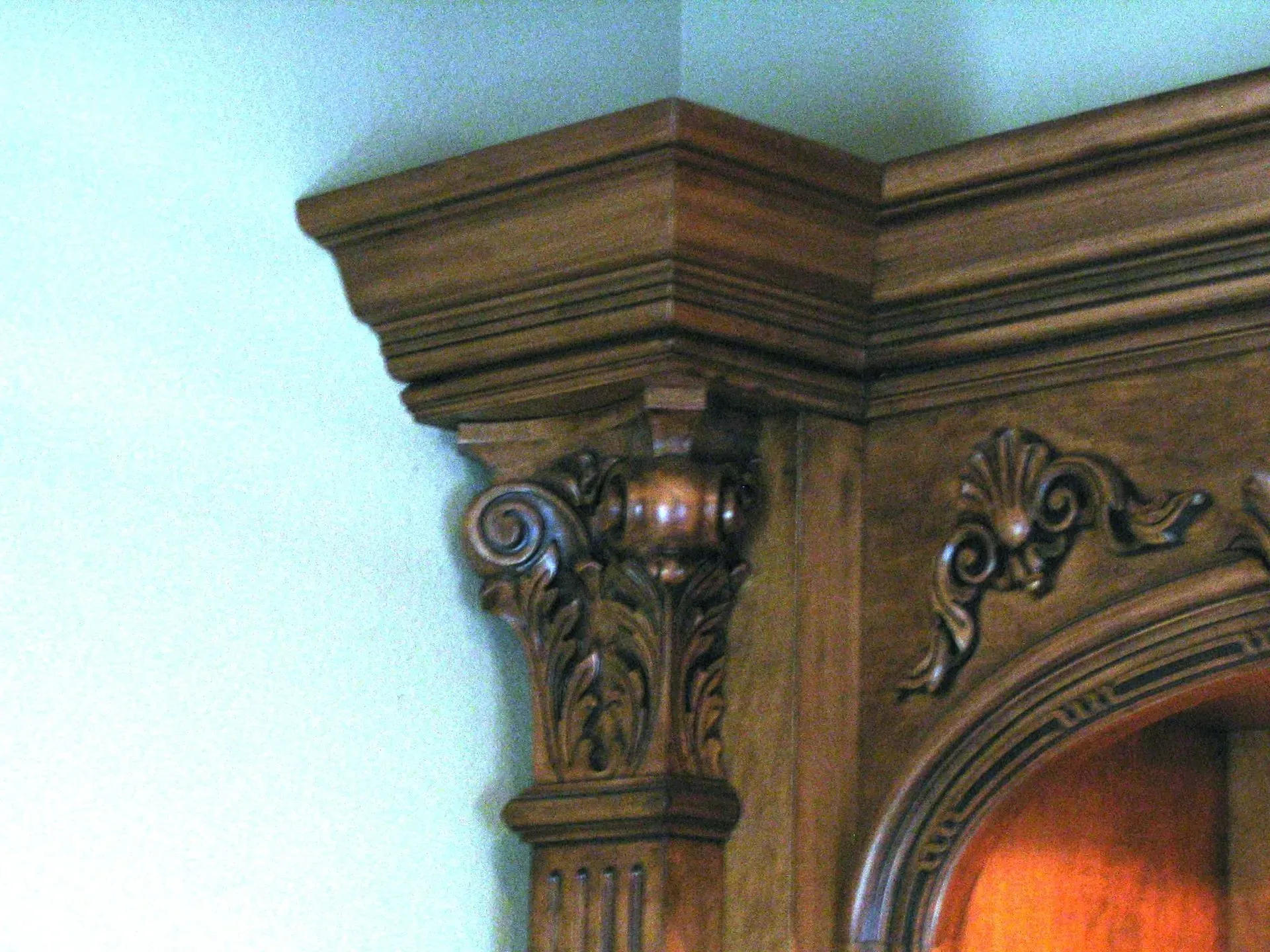 Ornate carved wooden mirror frame with decorative scrollwork and brown finish against a light blue wall