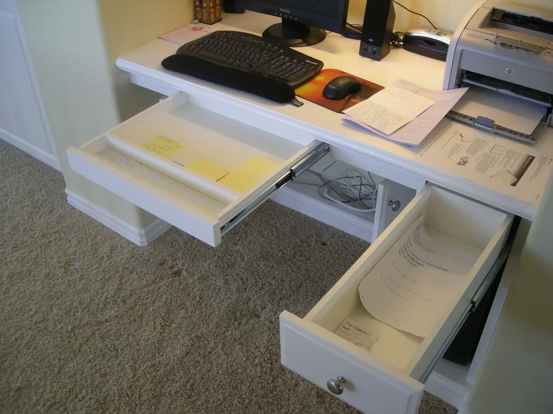 Office desk with computer, keyboard, papers, and open drawers in a carpeted room