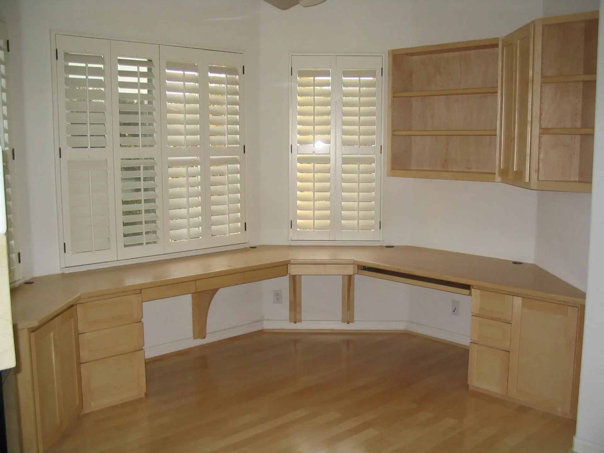 Empty room with built-in wooden desk and cabinets along a curved wall, hardwood floor, and plantation shutters