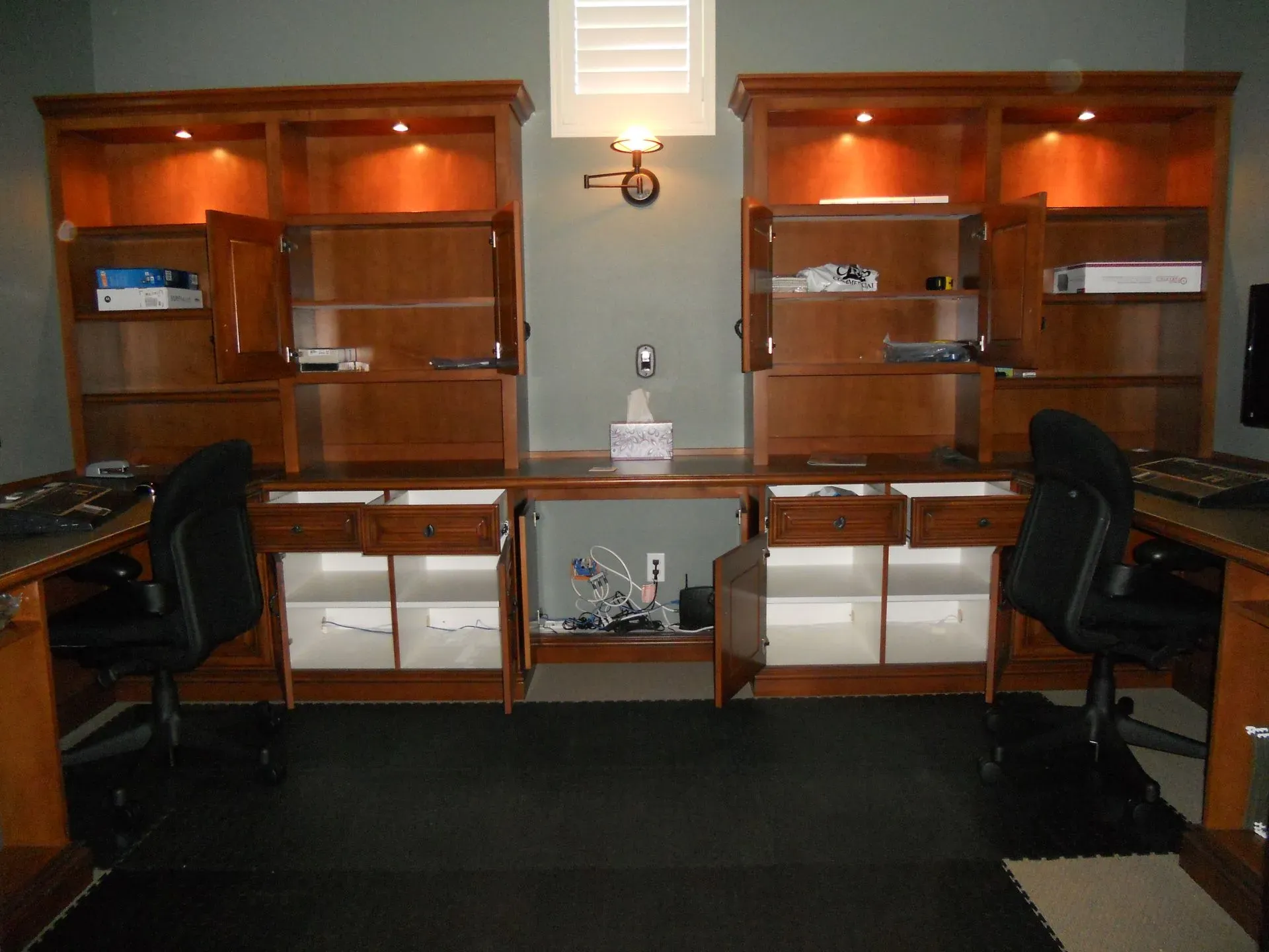 Wood-paneled lobby with two matching chairs, wall sconces, and built-in shelves and cabinets around a central niche