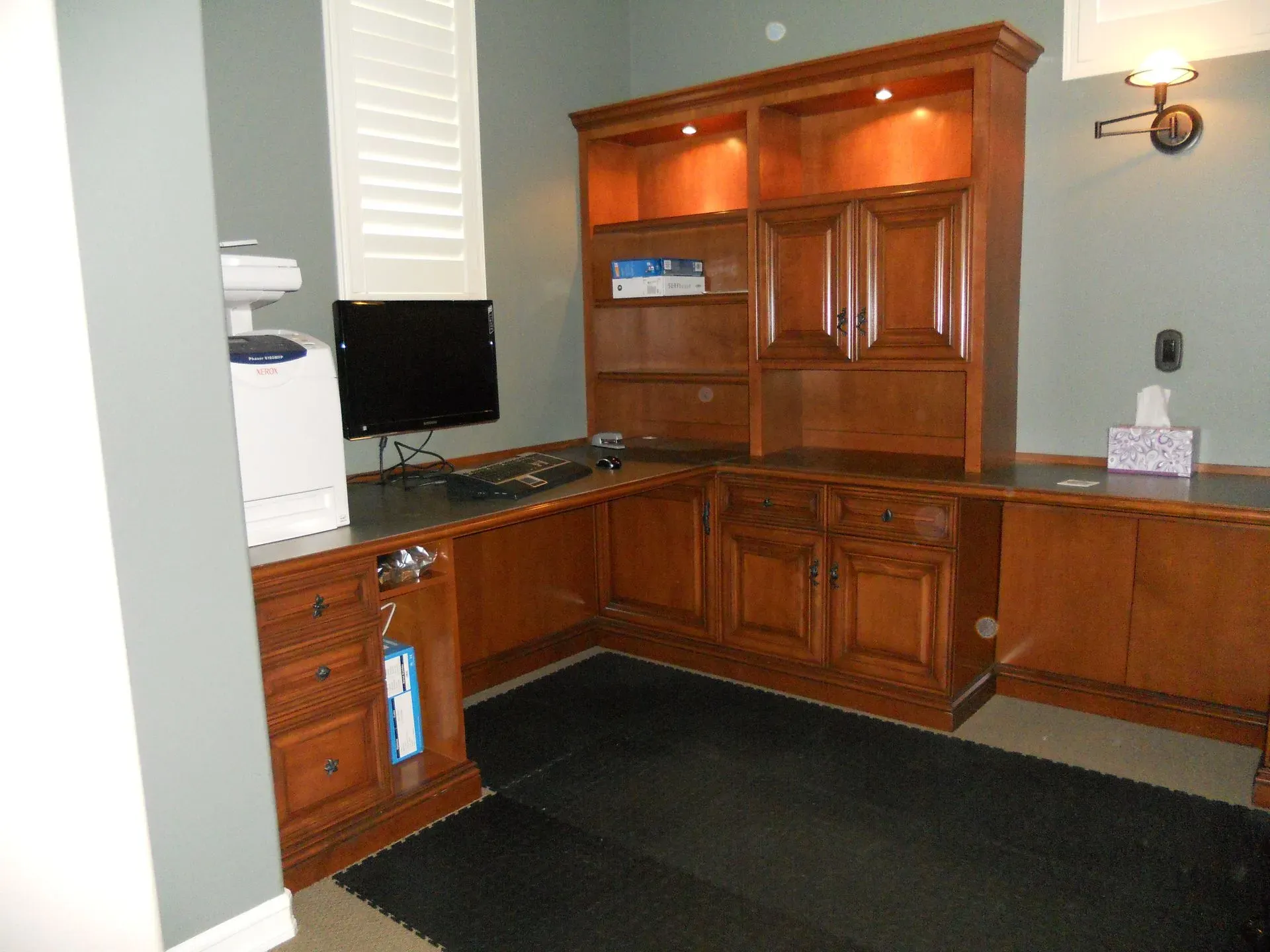 Built-in wooden office cabinets and shelving along a wall with black carpet flooring.