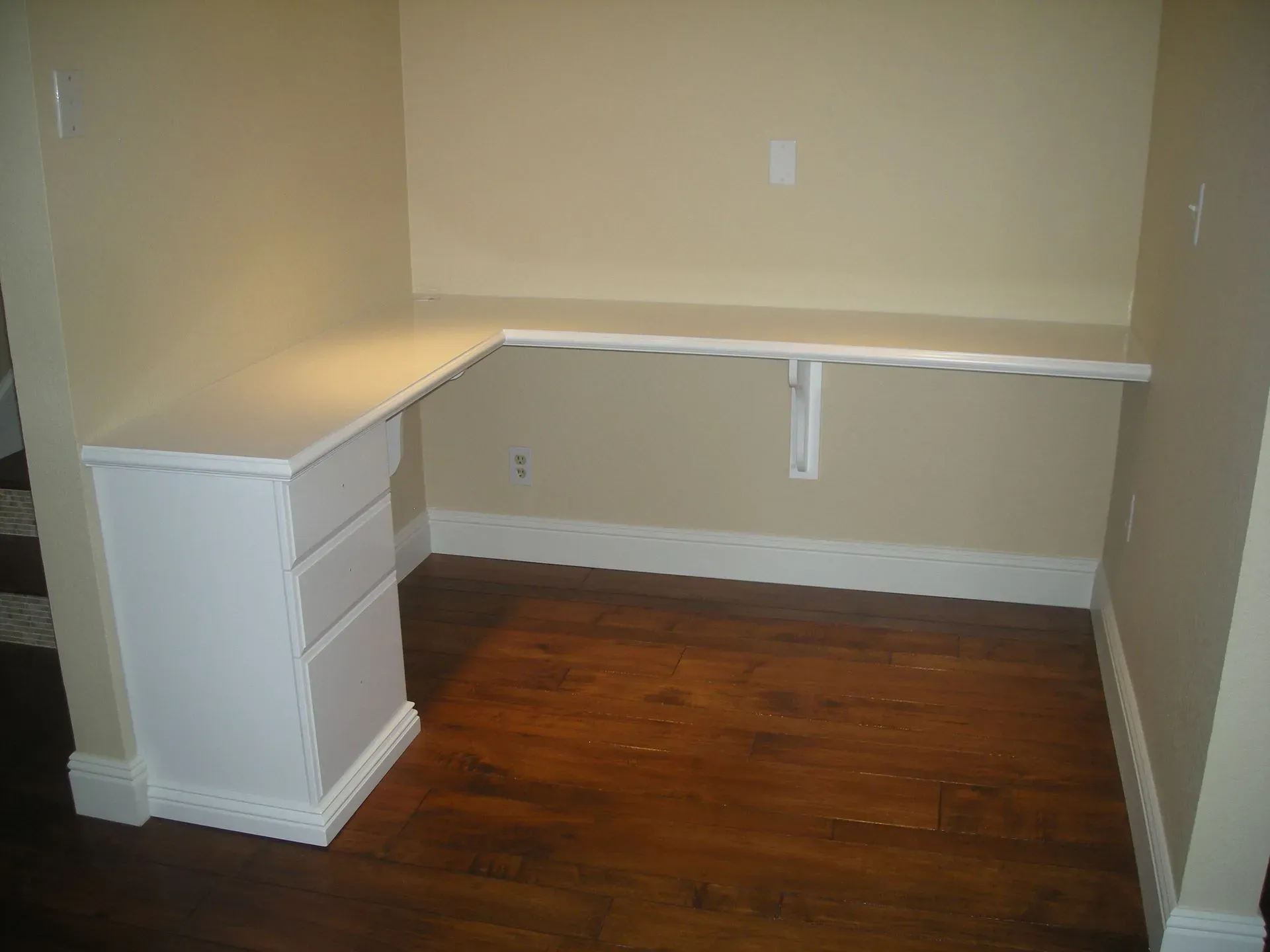 Empty home office nook with built-in white desk and drawers on hardwood floor