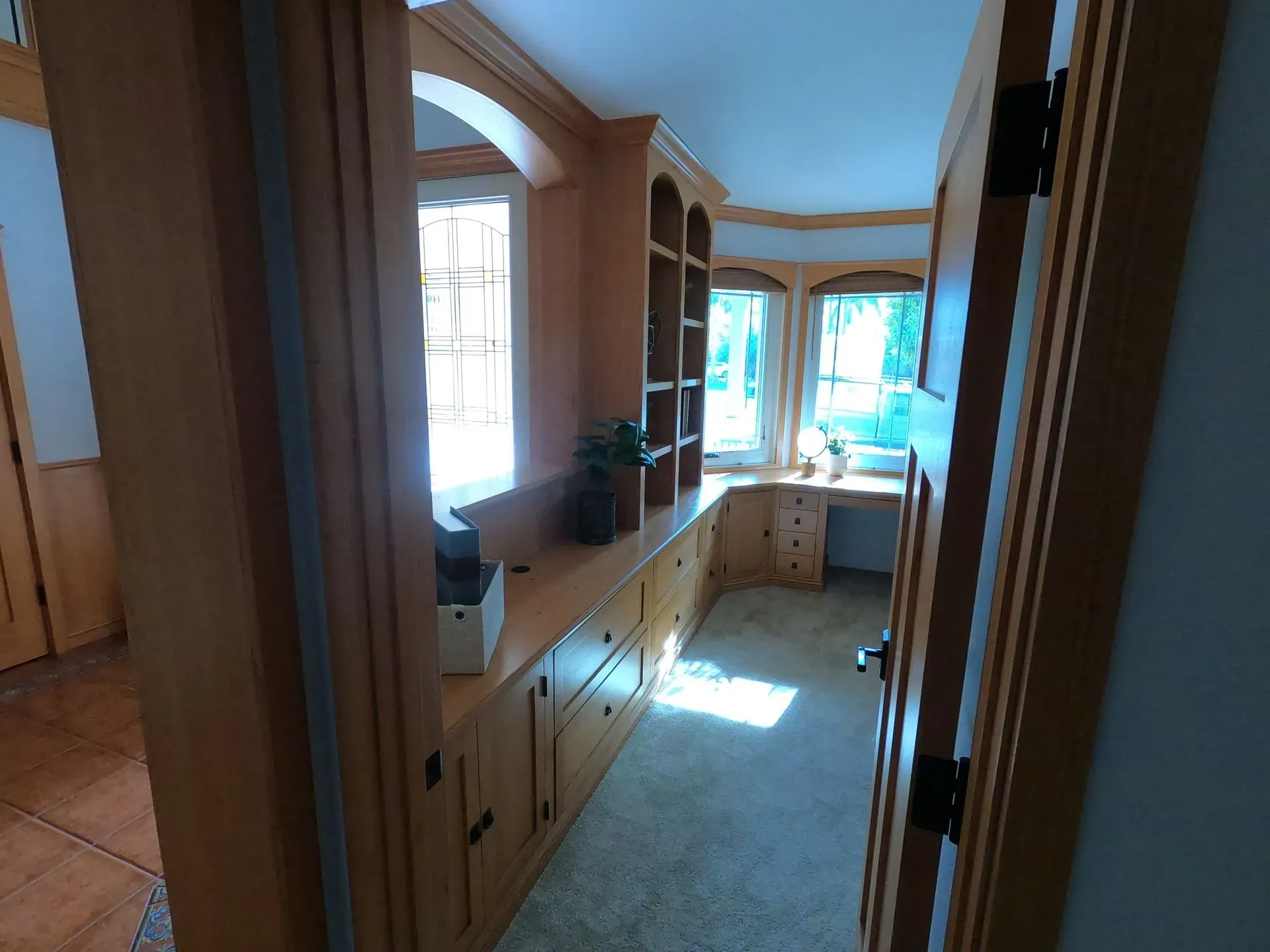 Narrow kitchen hallway with wood cabinets, bright windows, and a sunlit floor