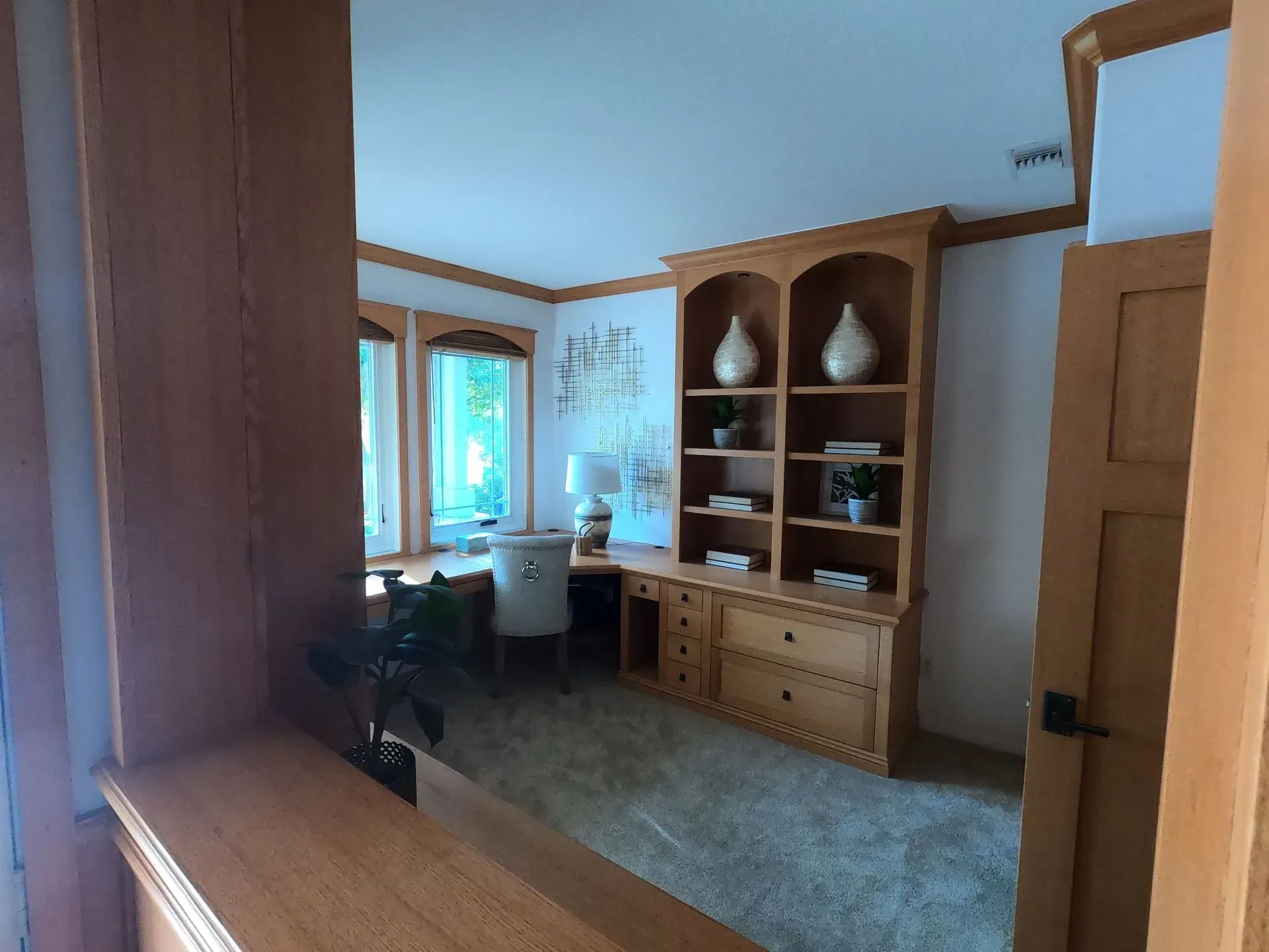 Bright living room with wood furniture, cabinets, and large windows overlooking a green view.