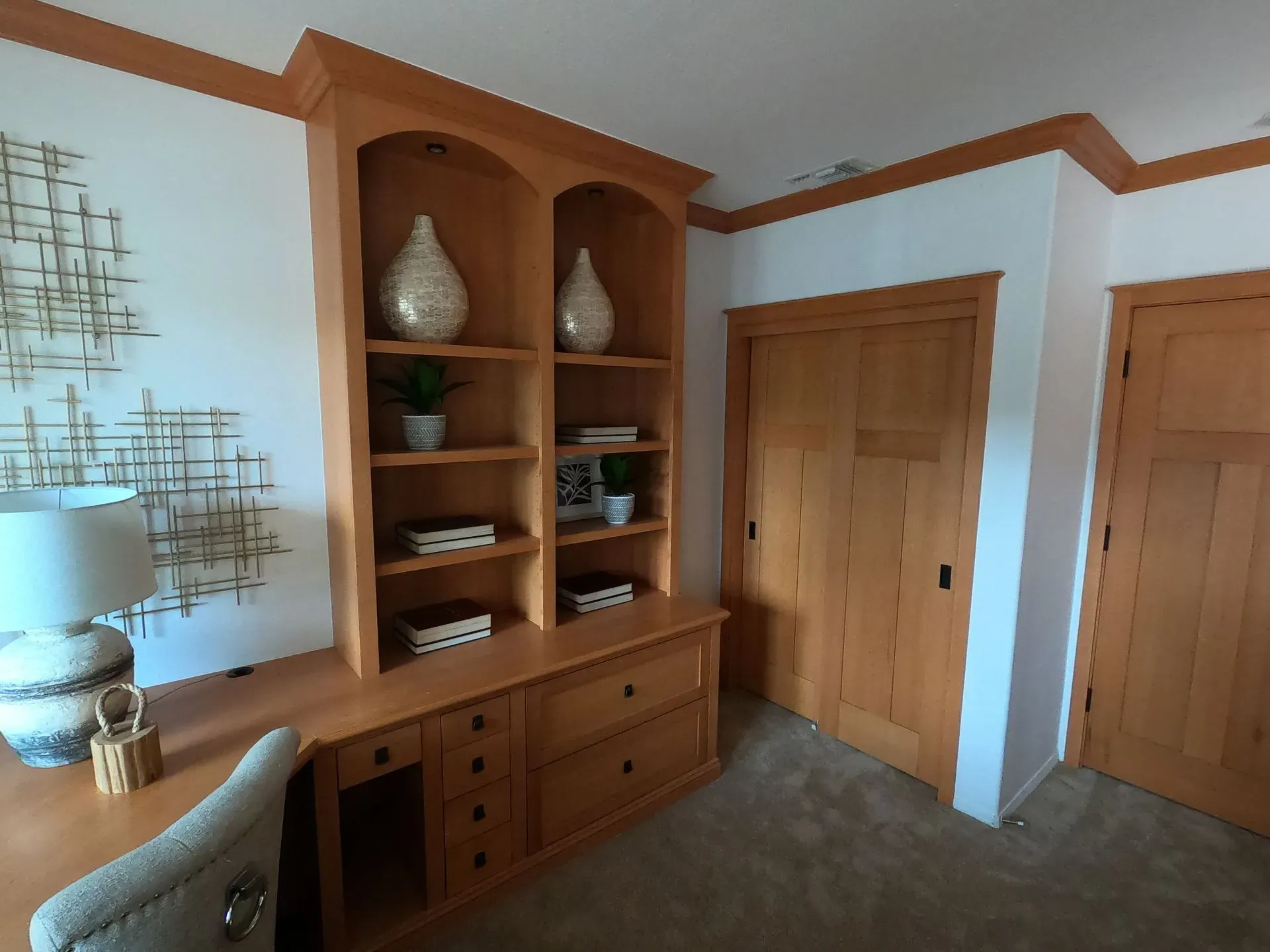 Built-in wooden cabinets and shelving in a carpeted room with white walls and orange trim.