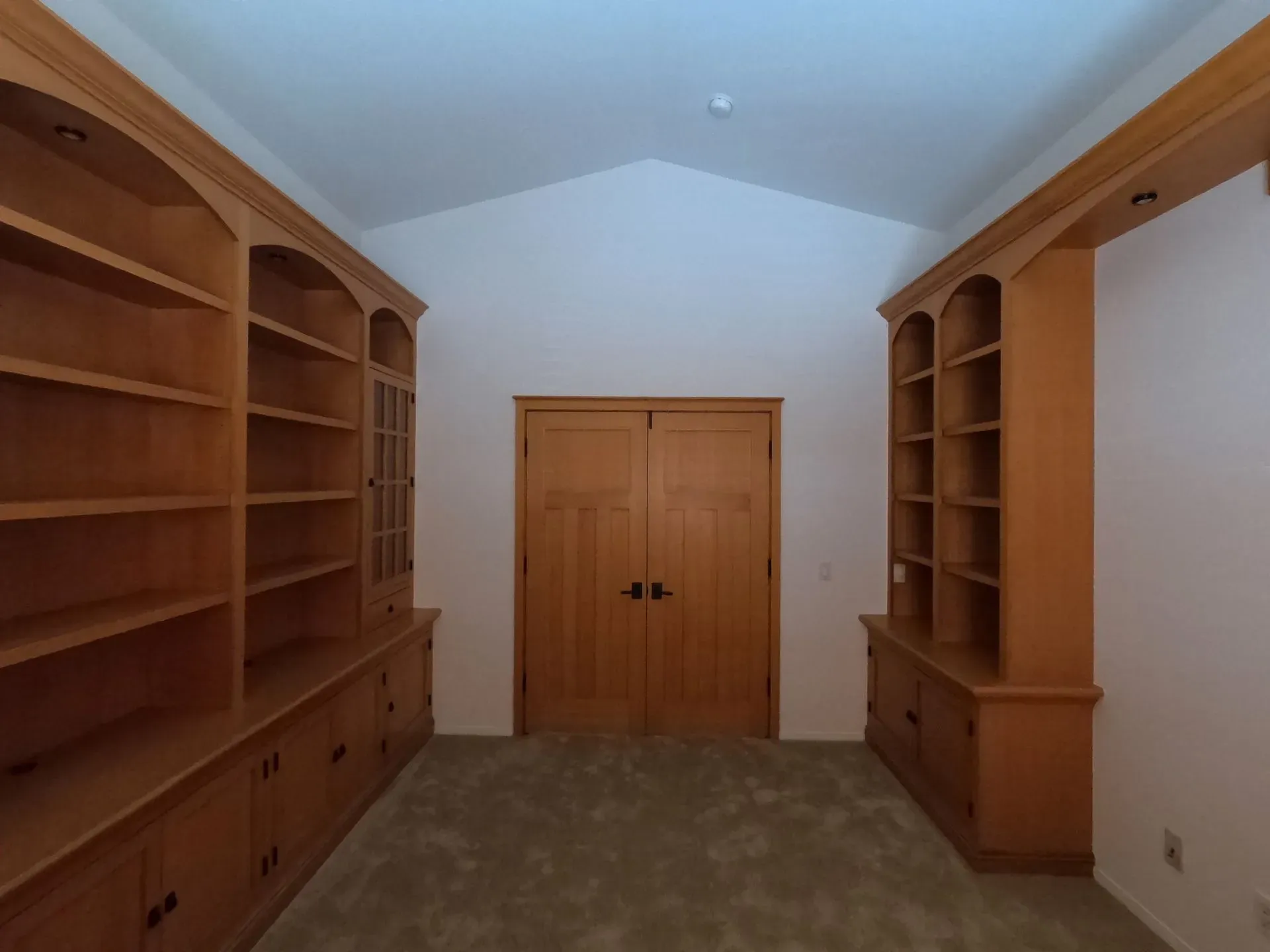 Spacious walk-in closet with wooden built-in shelves, cabinets, and double doors at the far end