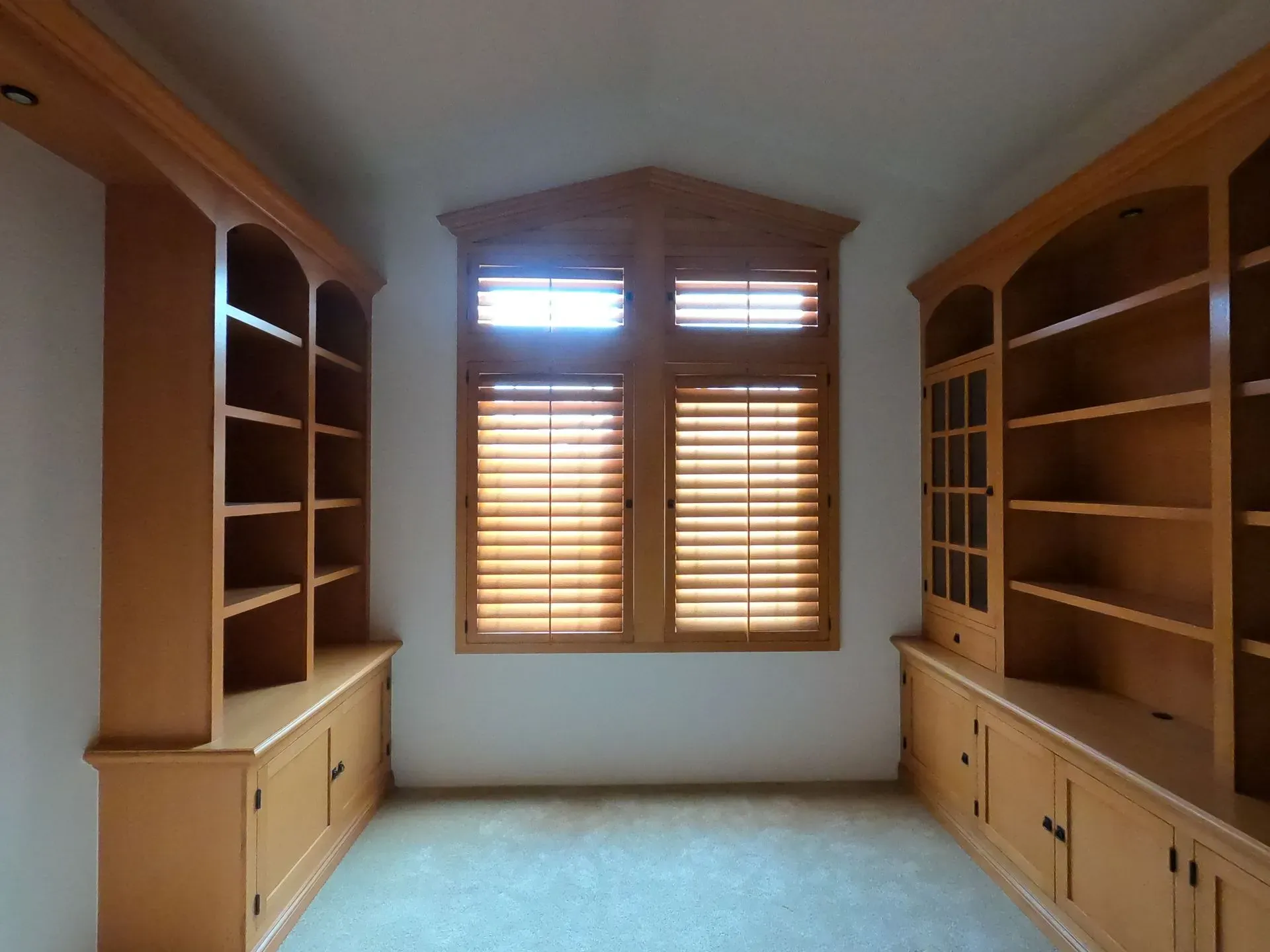 Built-in wooden bookshelves lining a bright room with a window and closed blinds at the far end