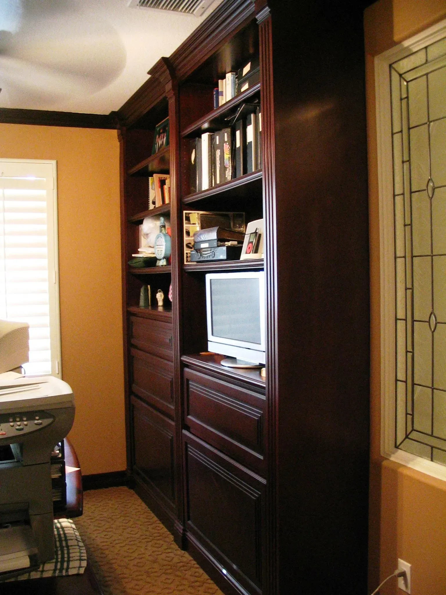 Dark wood built-in cabinet with shelves and a small TV in a narrow room near a window.