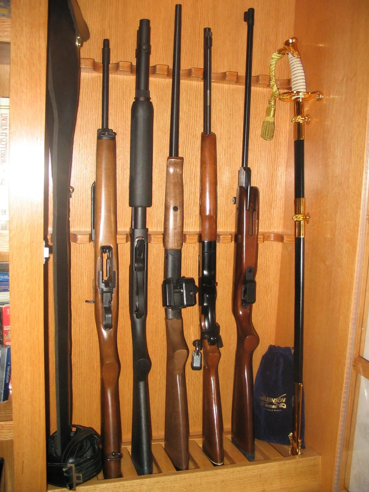 Rifles and shotguns standing upright in a wooden gun cabinet