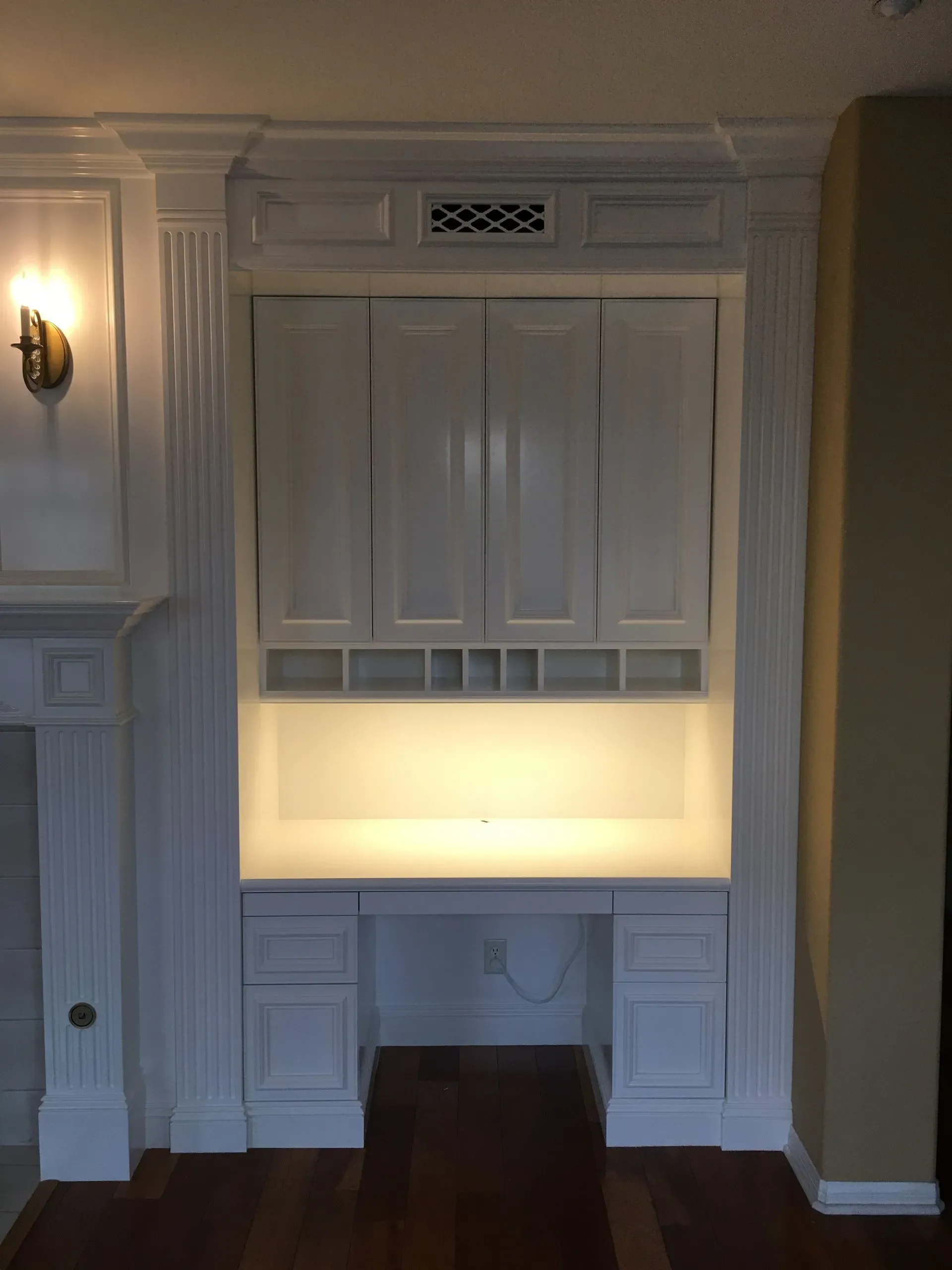 Built-in white cabinetry with illuminated niche and lower drawers in a paneled room.