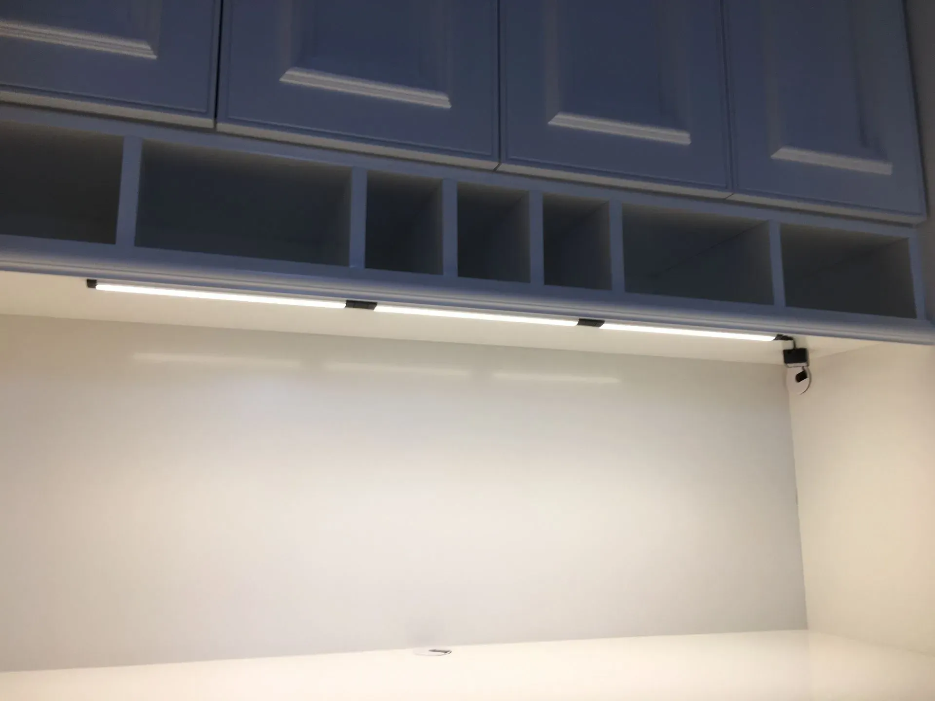 Empty whiteboard beneath blue cabinets with under-cabinet lights in a room