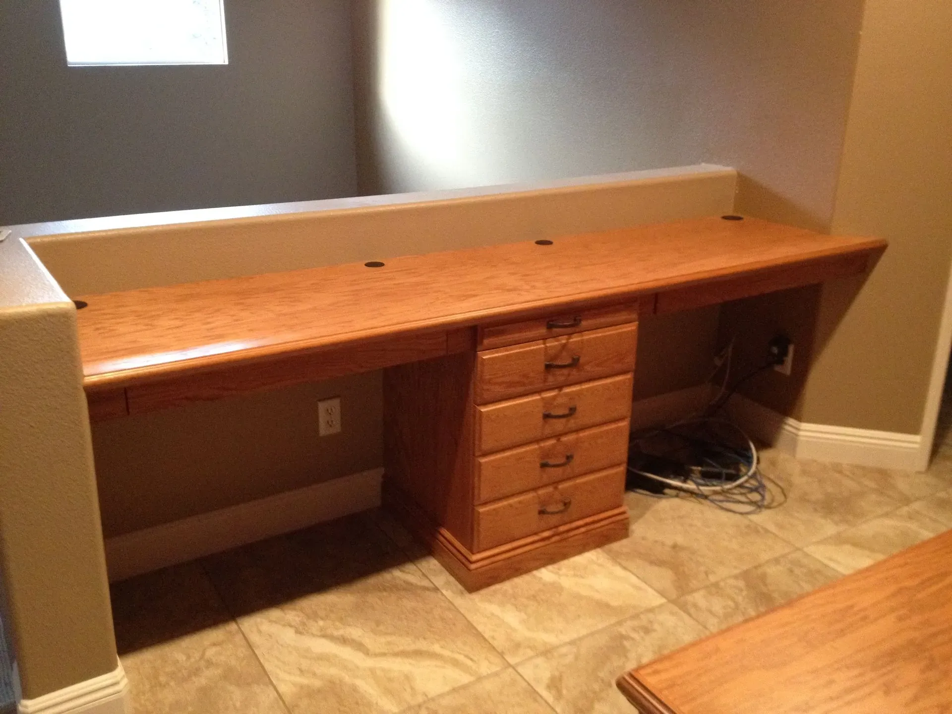 Long wooden built-in desk with drawers against a wall, with cords visible on the right side.